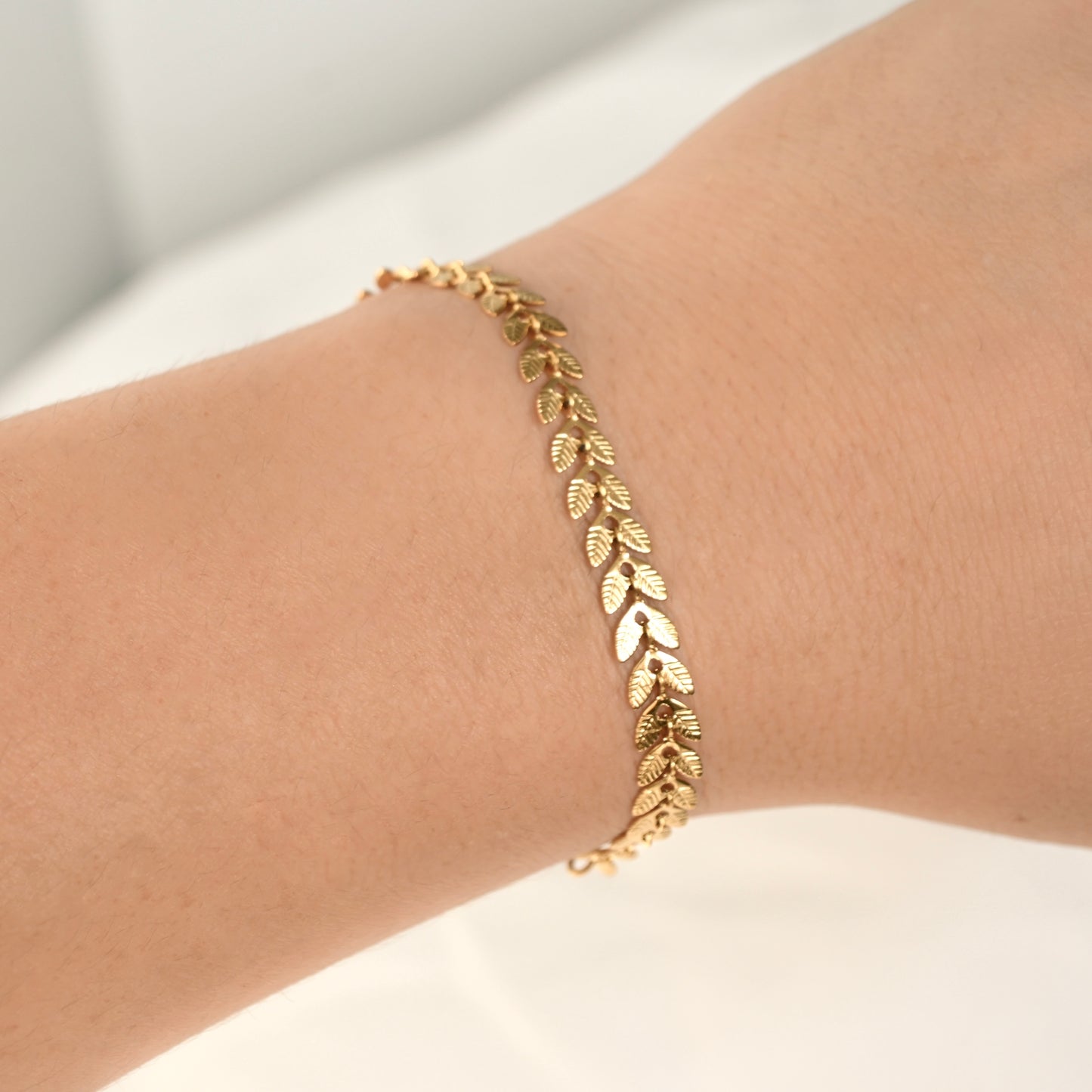 Gold bracelet with leaf patterns on a wrist against a neutral background