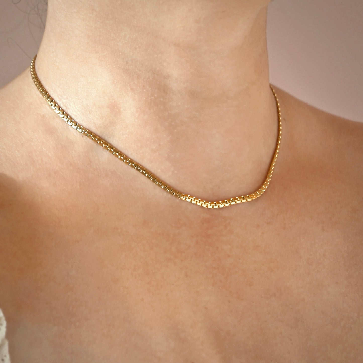 A bold gold chain necklace worn on a person's neck and upper chest, shown in a close-up shot against a soft neutral background.