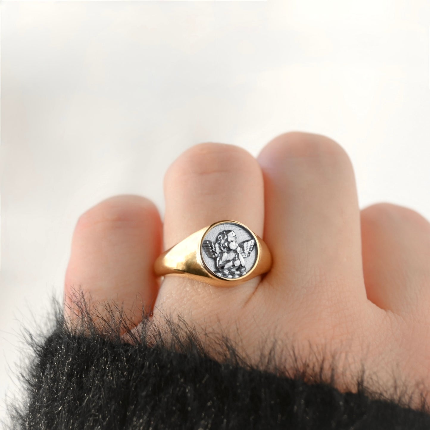 A close-up of a person's hand wearing a gold signet ring with a silver-toned circular medallion featuring a saint's portrait.