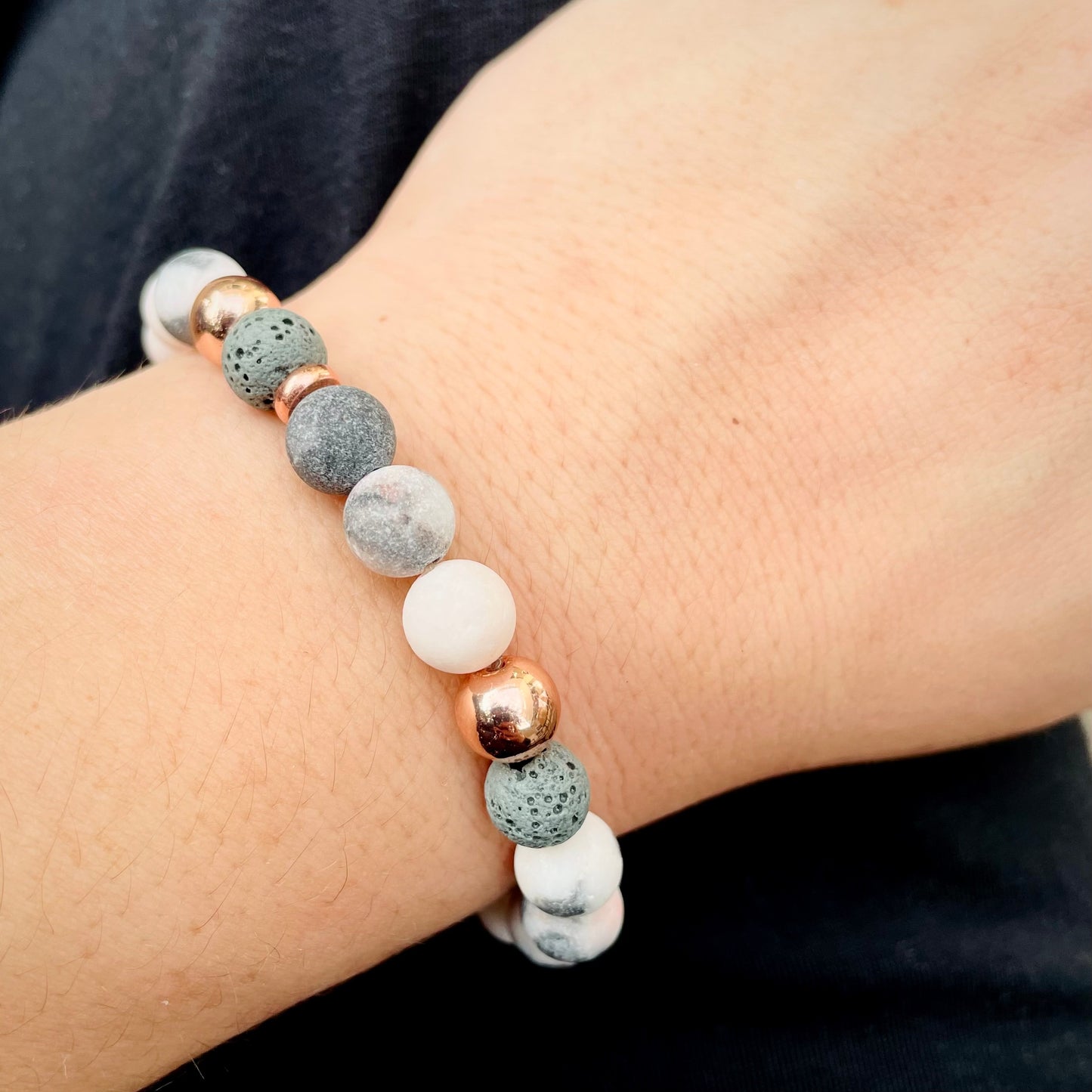 Bracelet with gray, white, and rose gold beads and stones on a wrist against a dark background