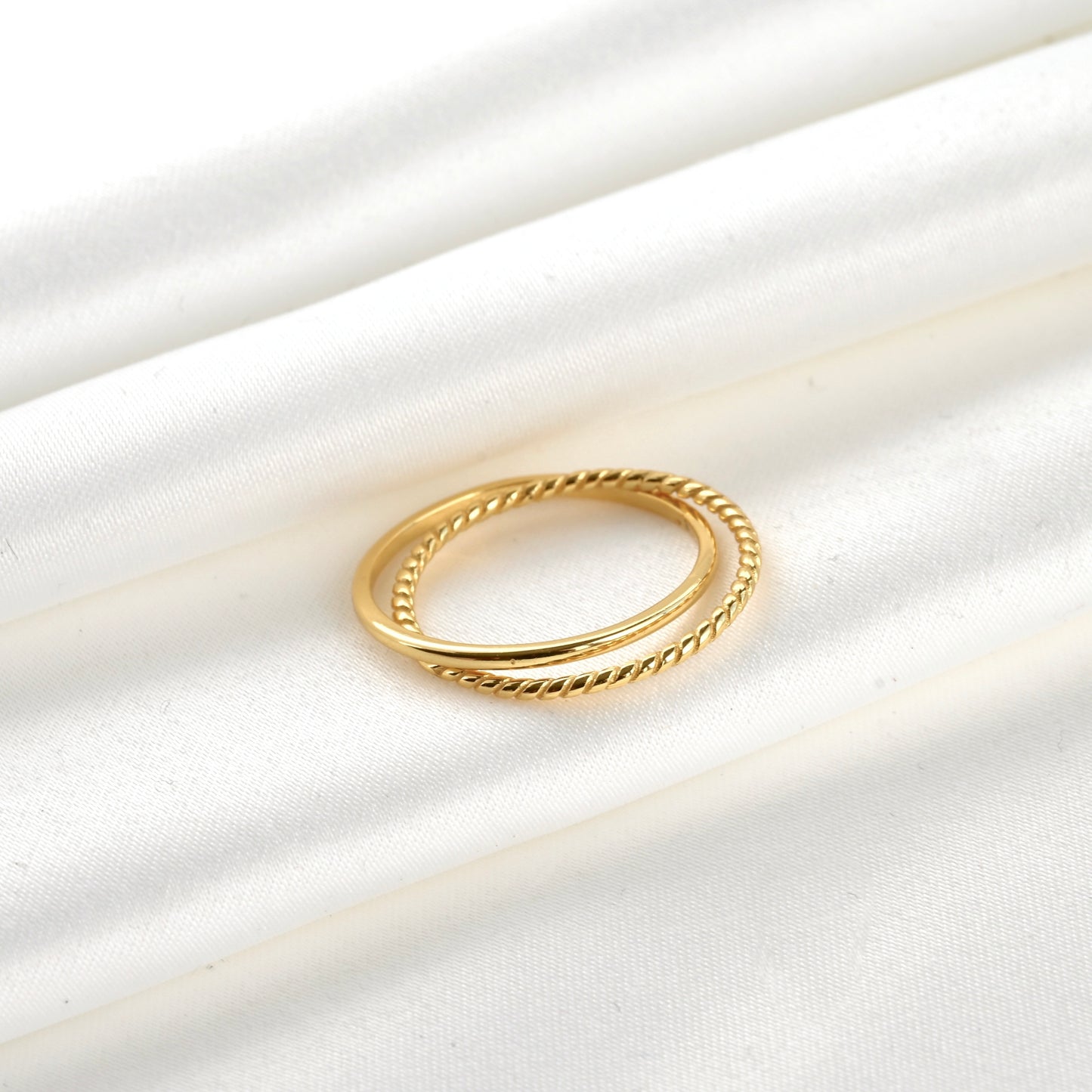 Dainty gold entwined bands ring on a white satin background
