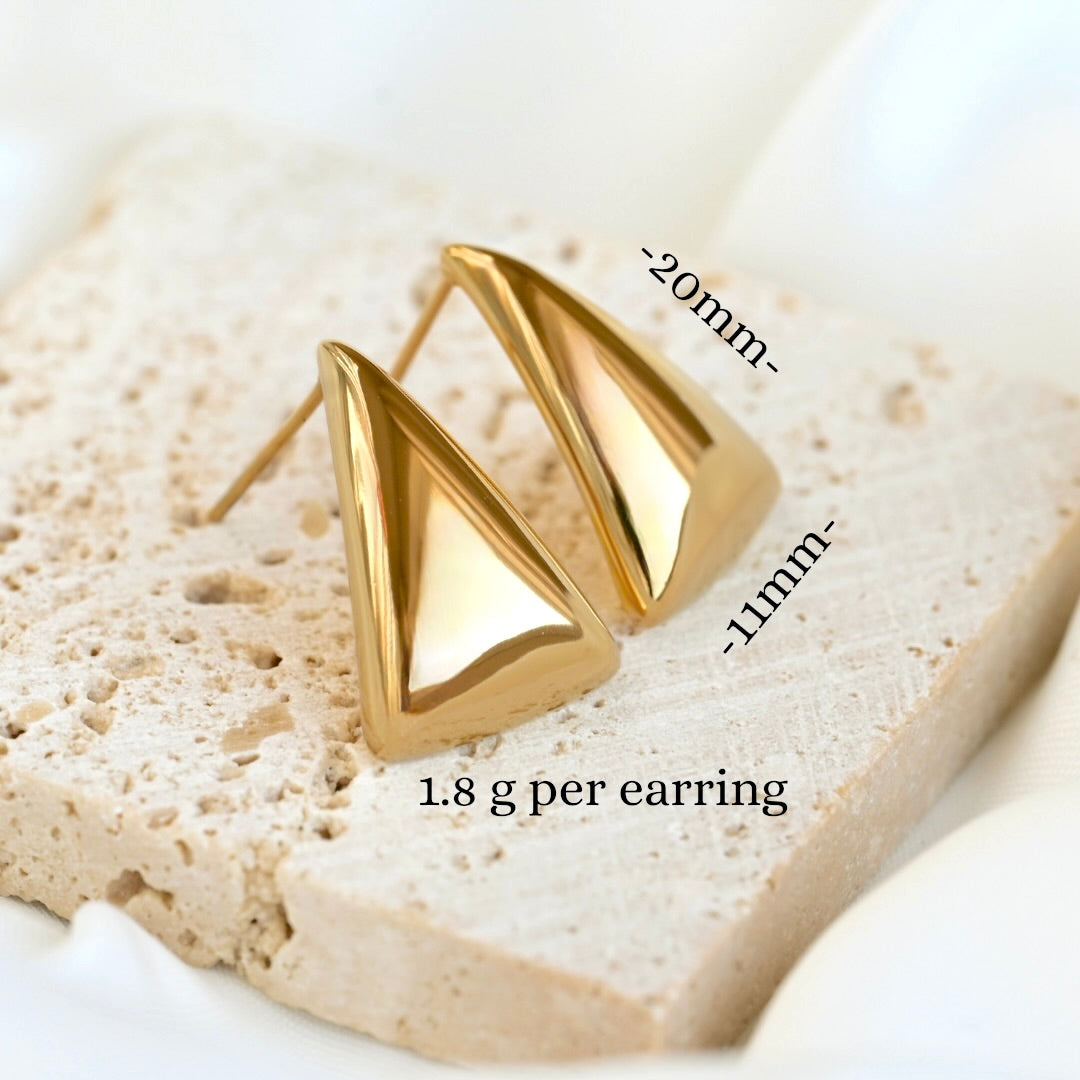 Gold triangle stud earrings on a textured stoe with measurements and weight information.