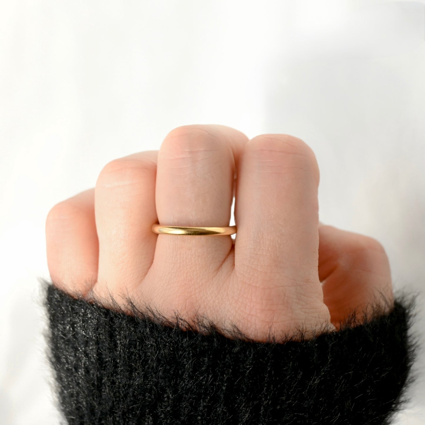 Hand with a fuzzy black sleeve wearing a slim rounded gold ring on middle finger  