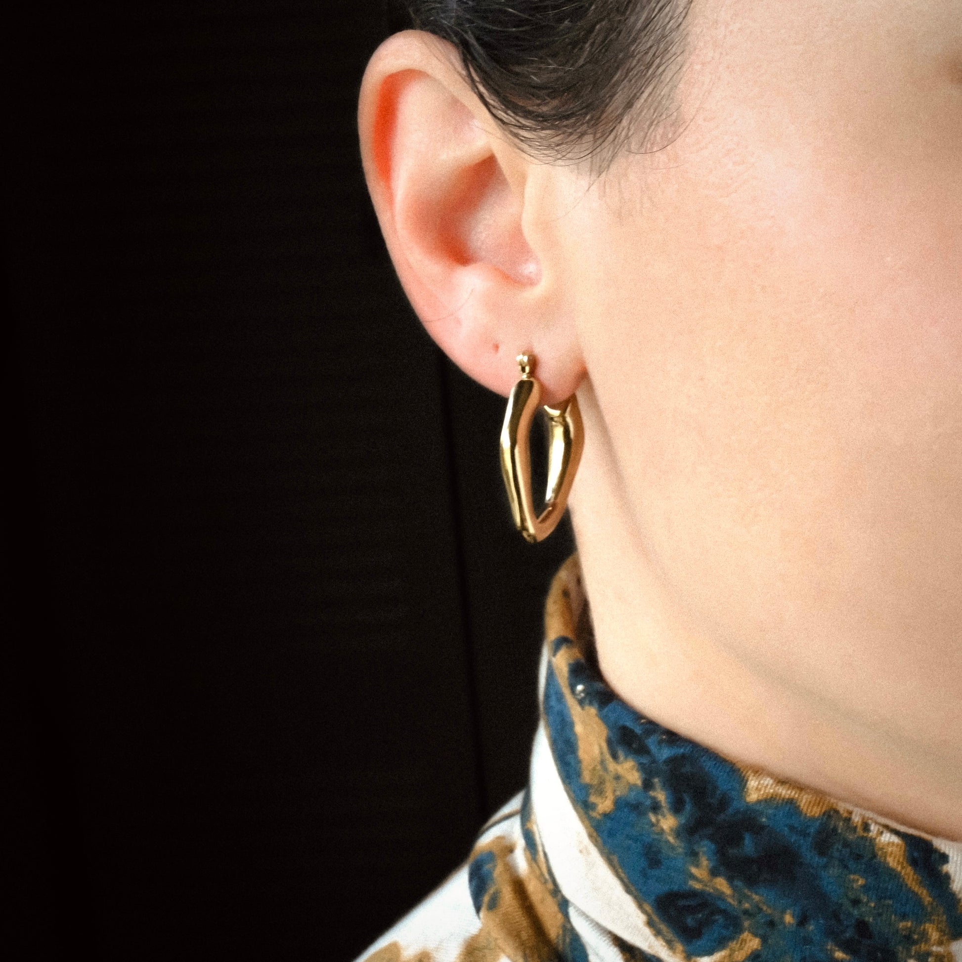 Gold figure hoop earrings worn by a person with a dark background
