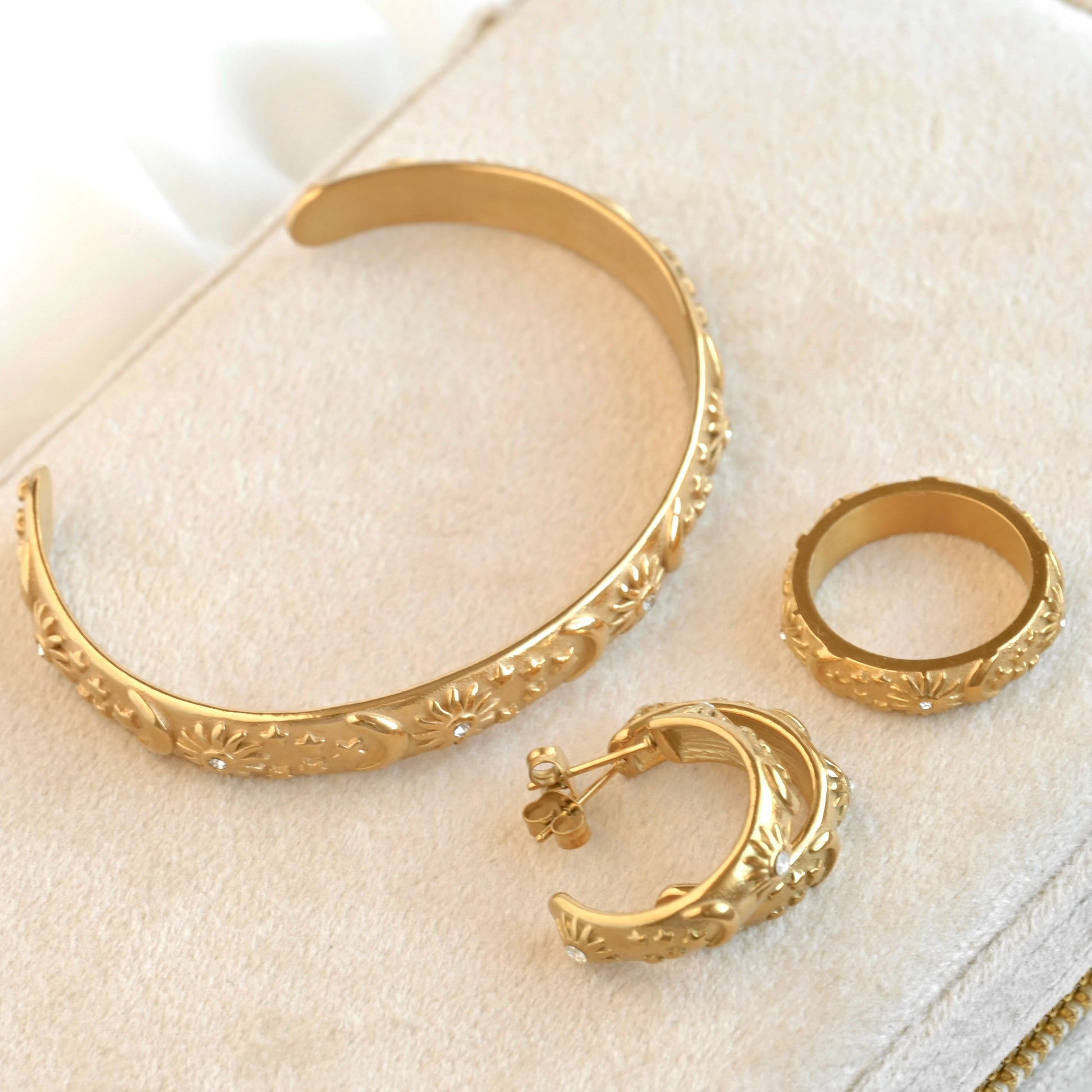 Gold bracelet, ring, and hoop earrings on a light beige surface