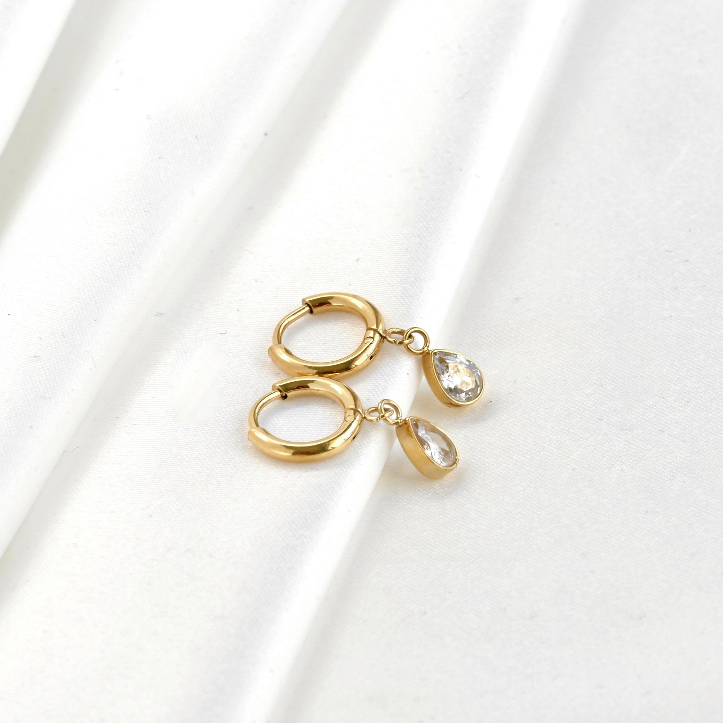 Wide angle view of Gold teardrop diamond charm earrings on a white background