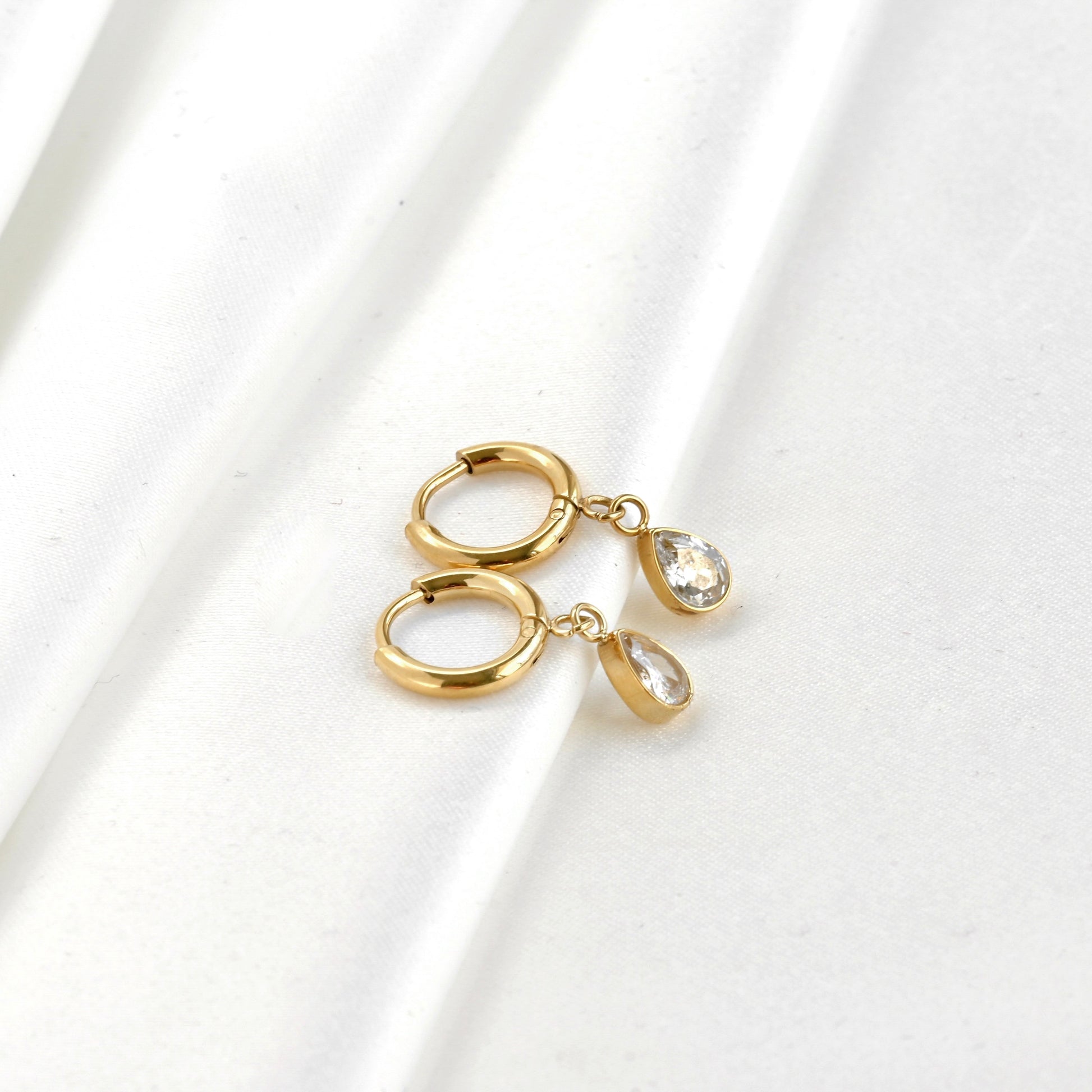 Wide angle view of Gold teardrop diamond charm earrings on a white background