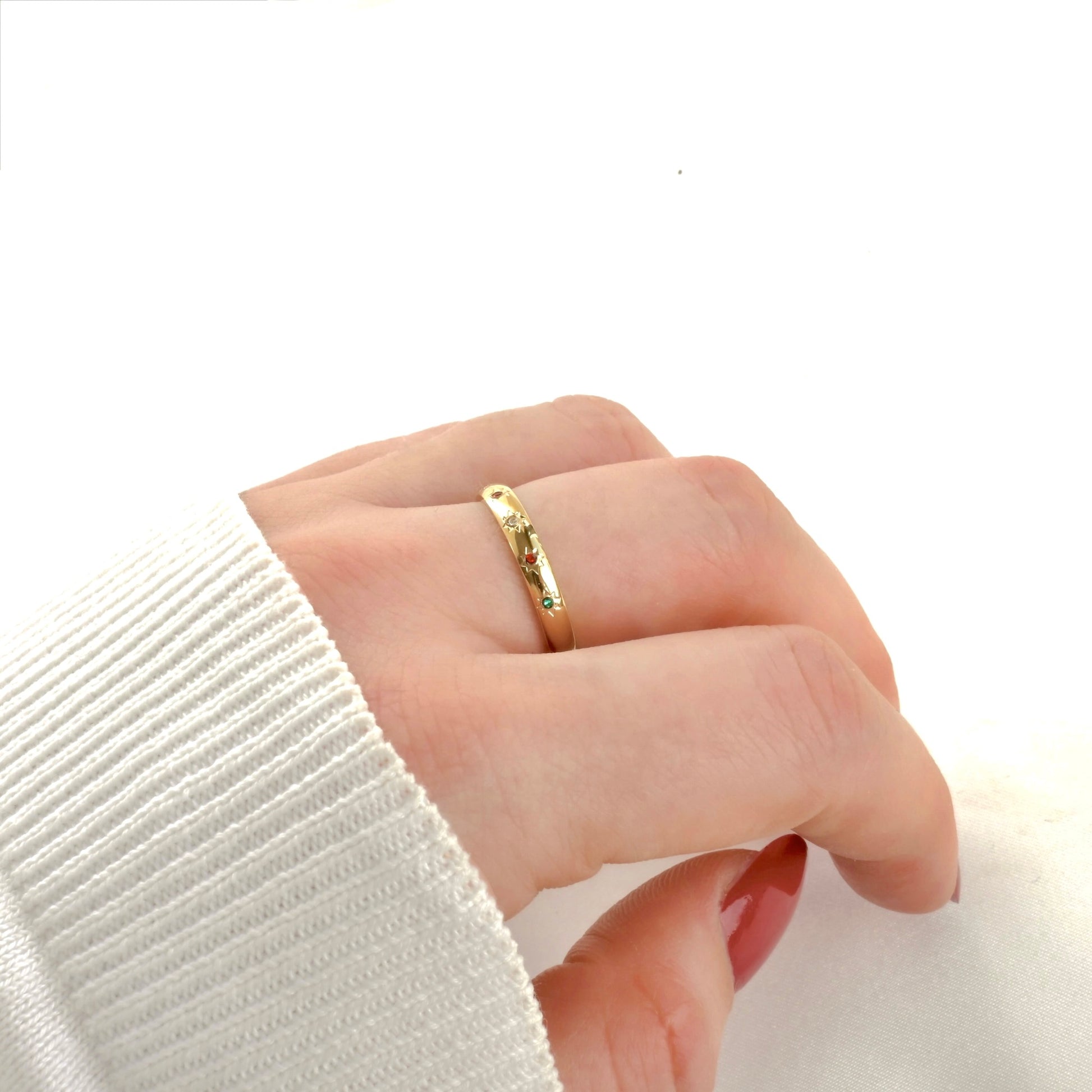 Slim gold star band with colorful stones on a person's finger with a white sleeve against a light background