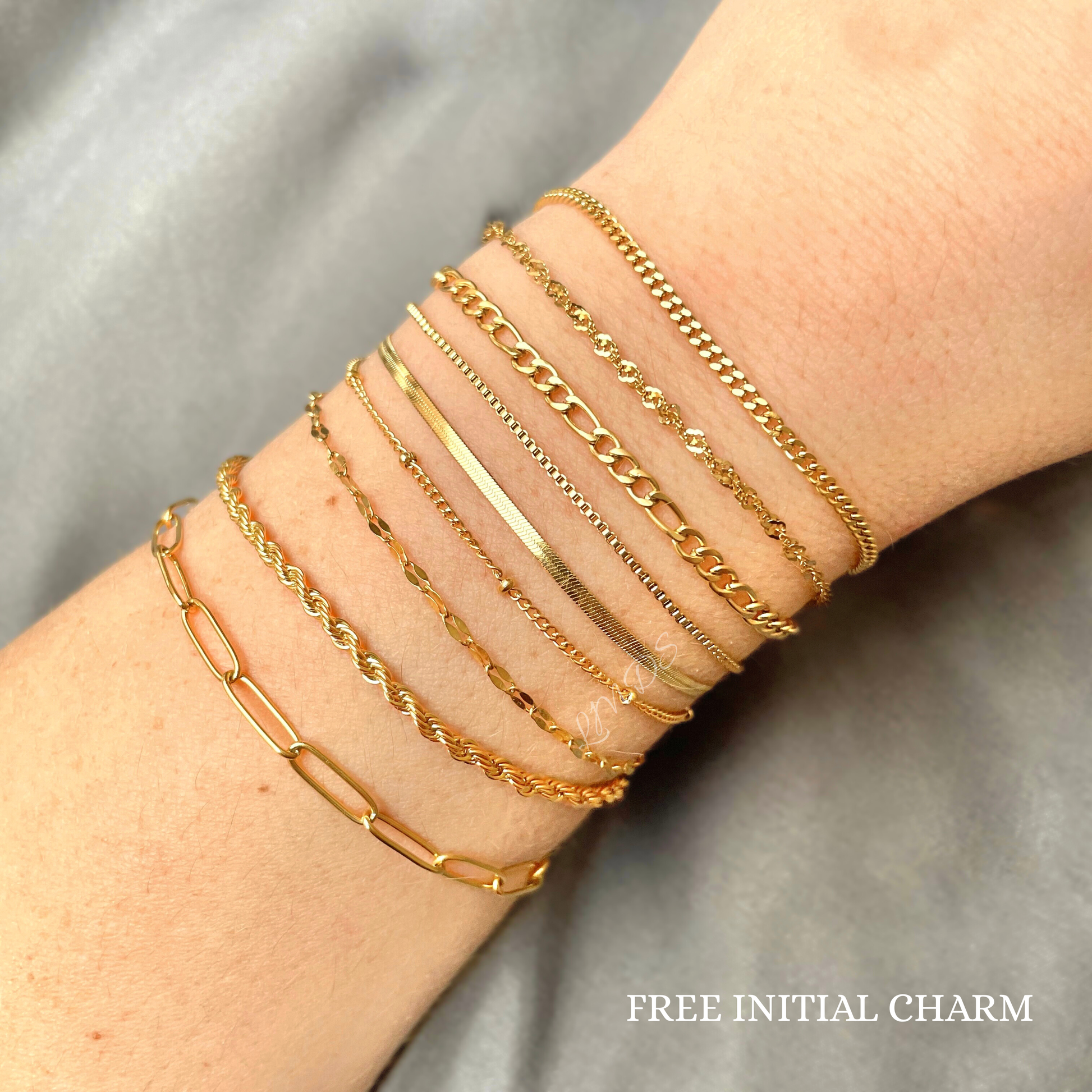 Thin rope bracelet stacked with eight other chain types on a wrist with a gray background