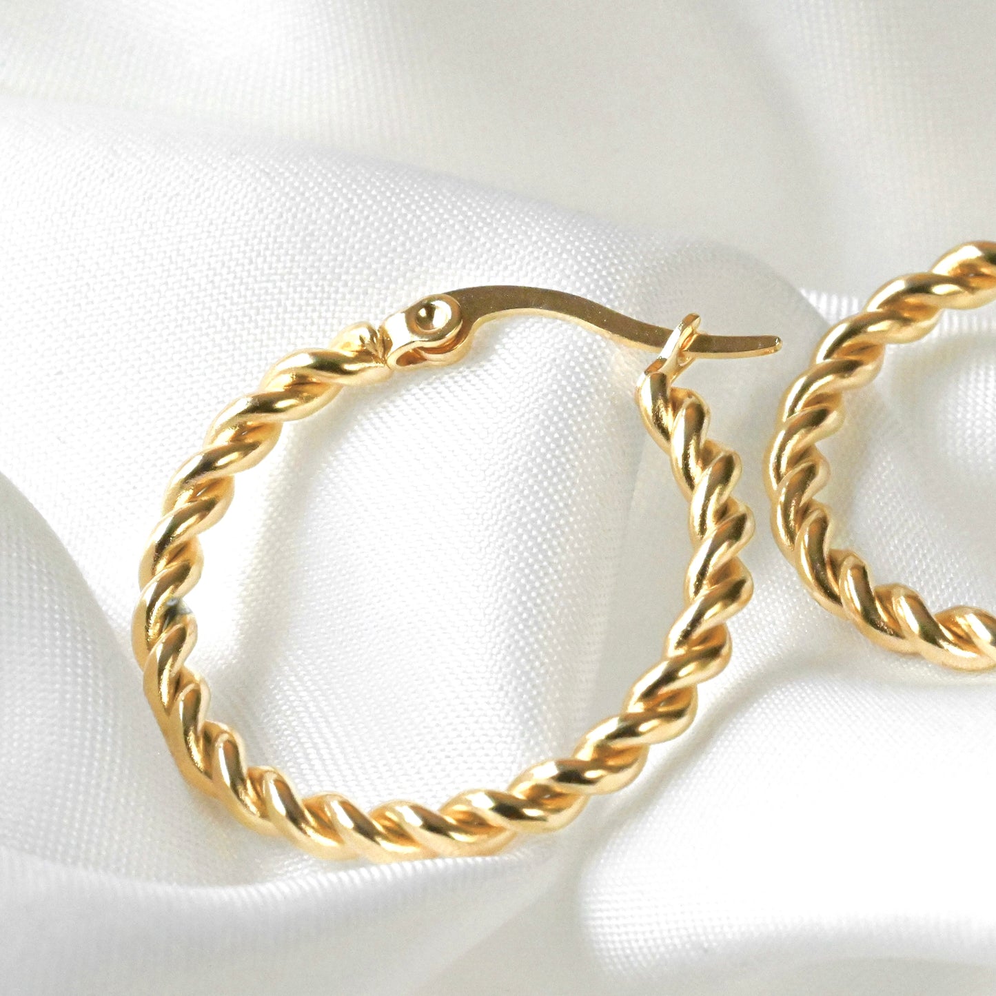 Gold hoop earrings on a white fabric background