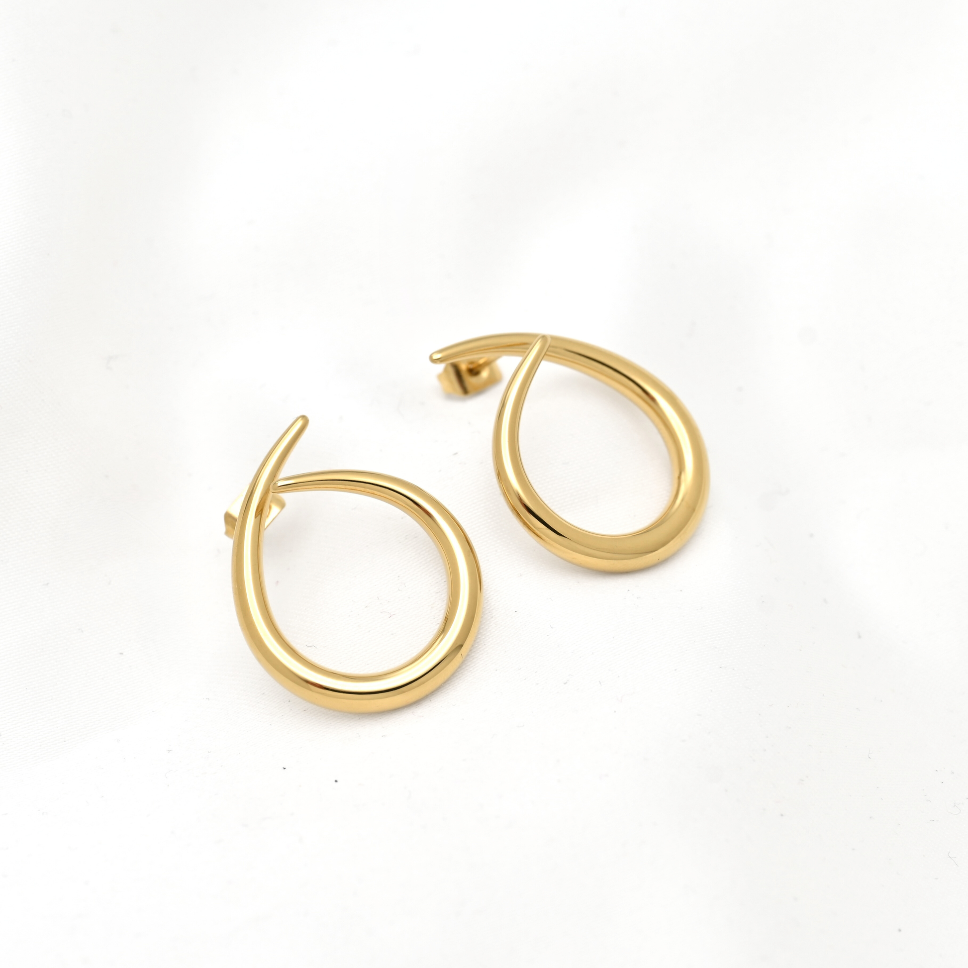A pair of gold hoop earrings with a modern, curved open design, displayed on a clean white background.