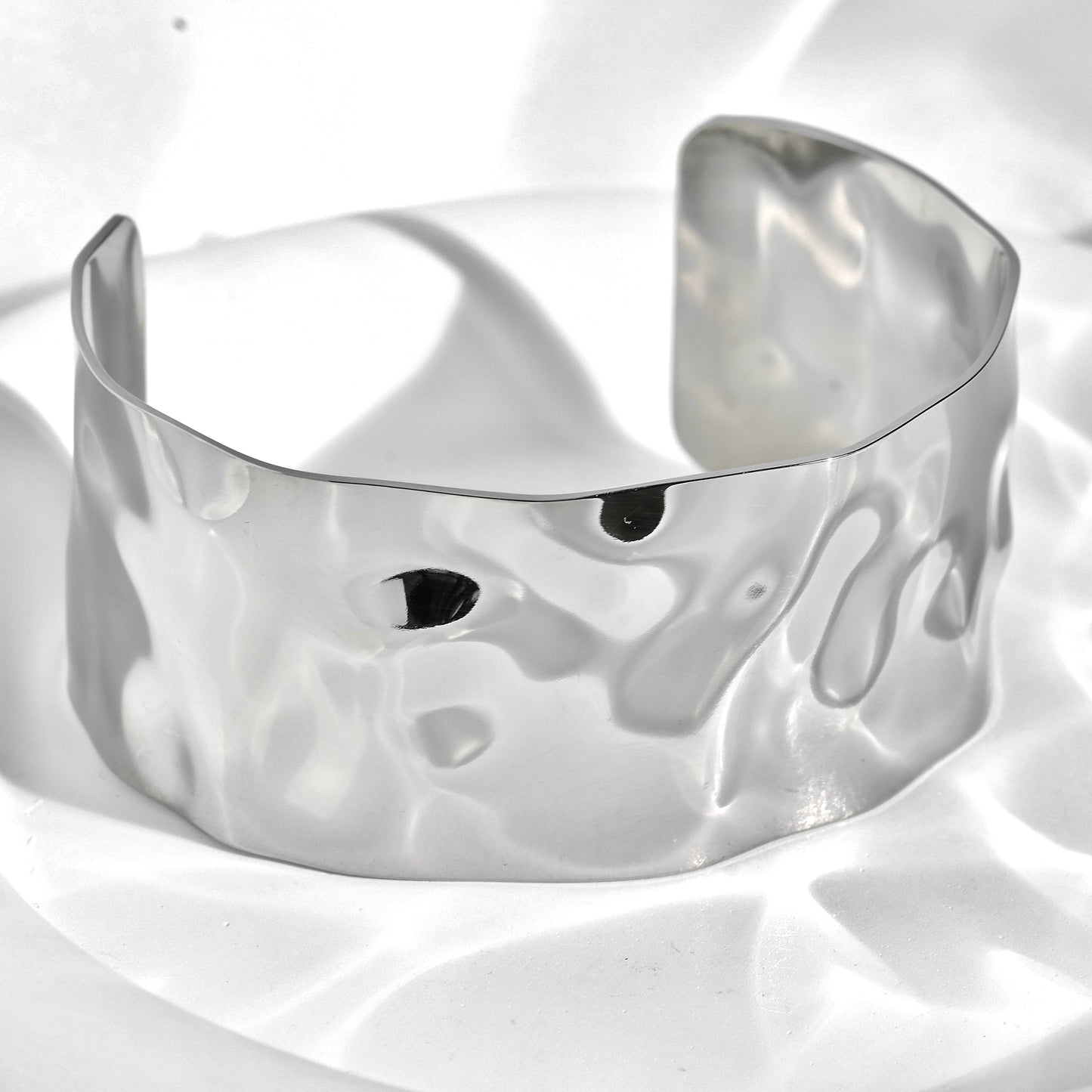 Silver cuff bracelet with a wavy texture on a white background