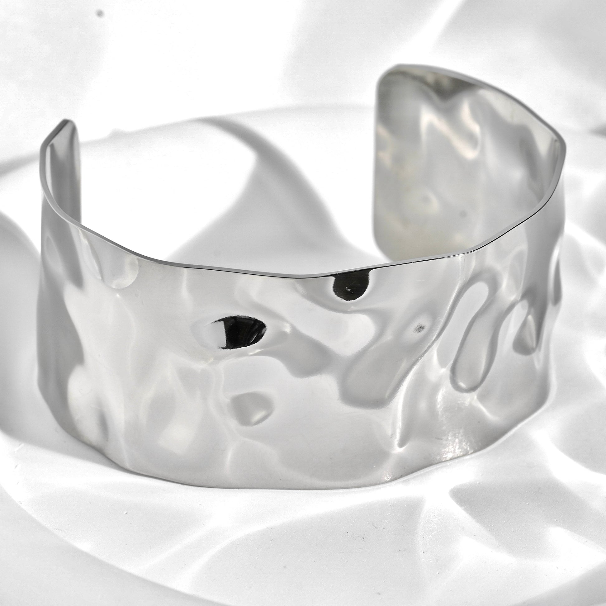 Silver cuff bracelet with a wavy texture on a white background