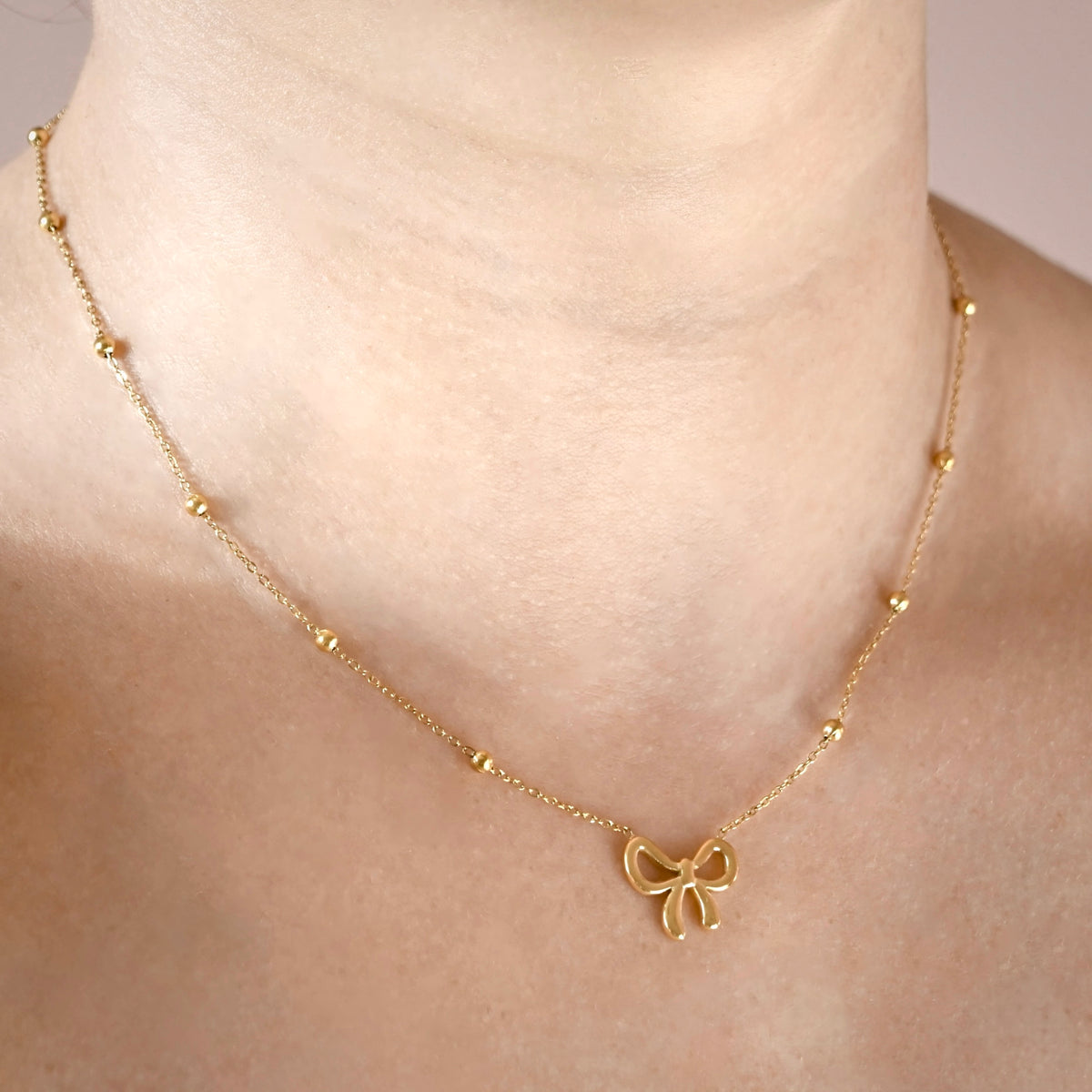 A delicate gold satellite chain necklace  with a bow-shaped pendant, shown worn on a model's neck.