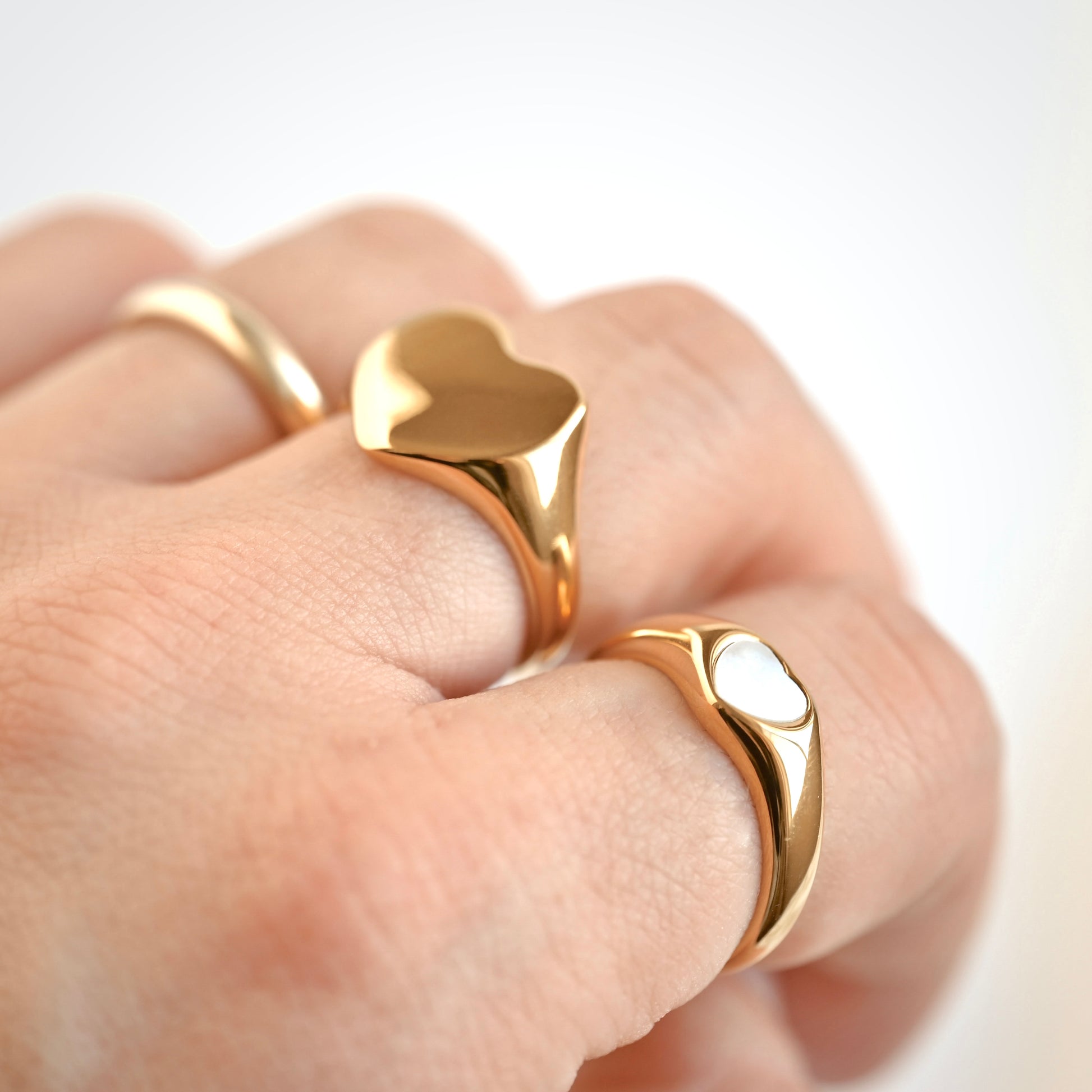 Gold pearl and signet style heart-shaped rings on a finger with a plain background