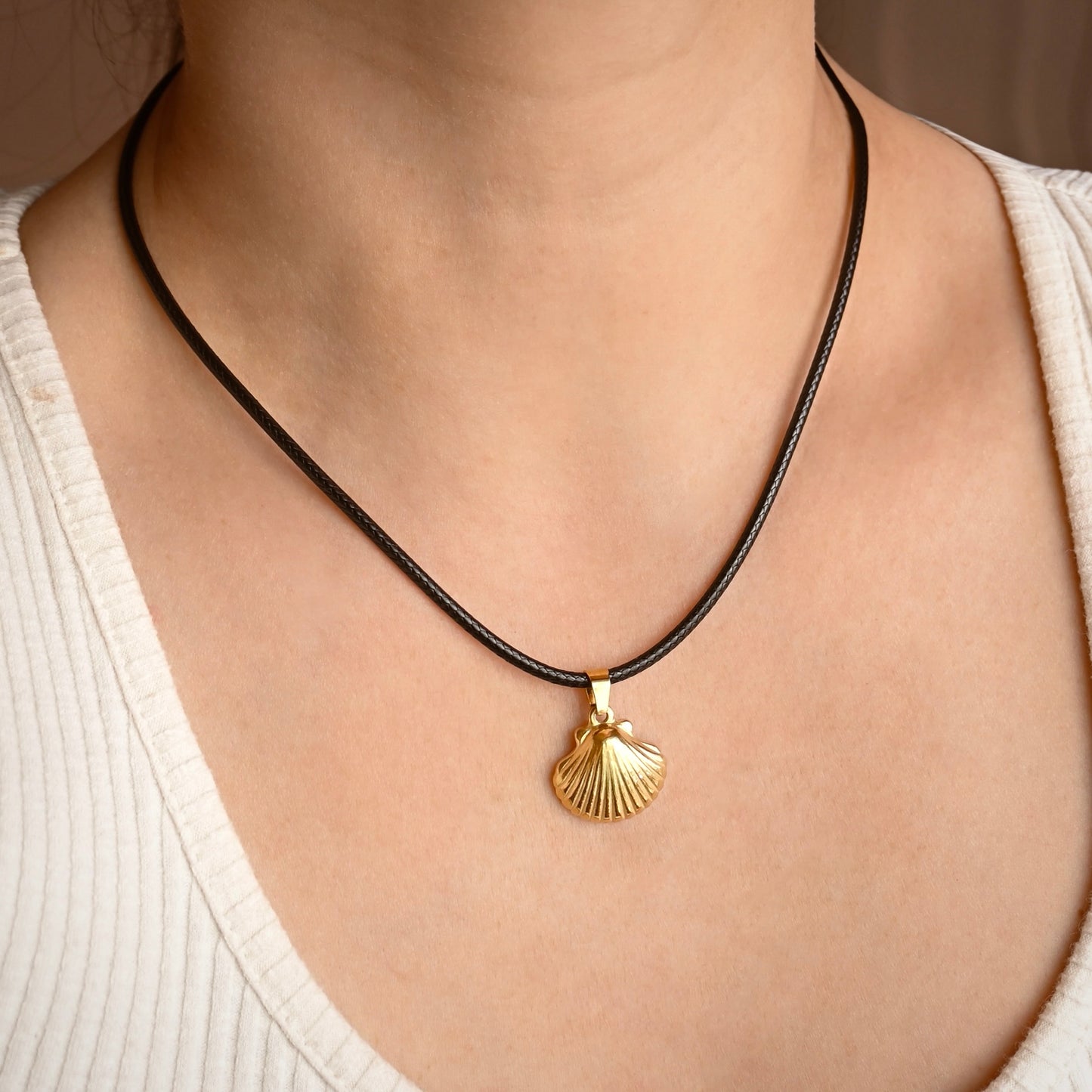 A close-up of a person wearing a thick black cord necklace with a gold shell-shaped pendant.