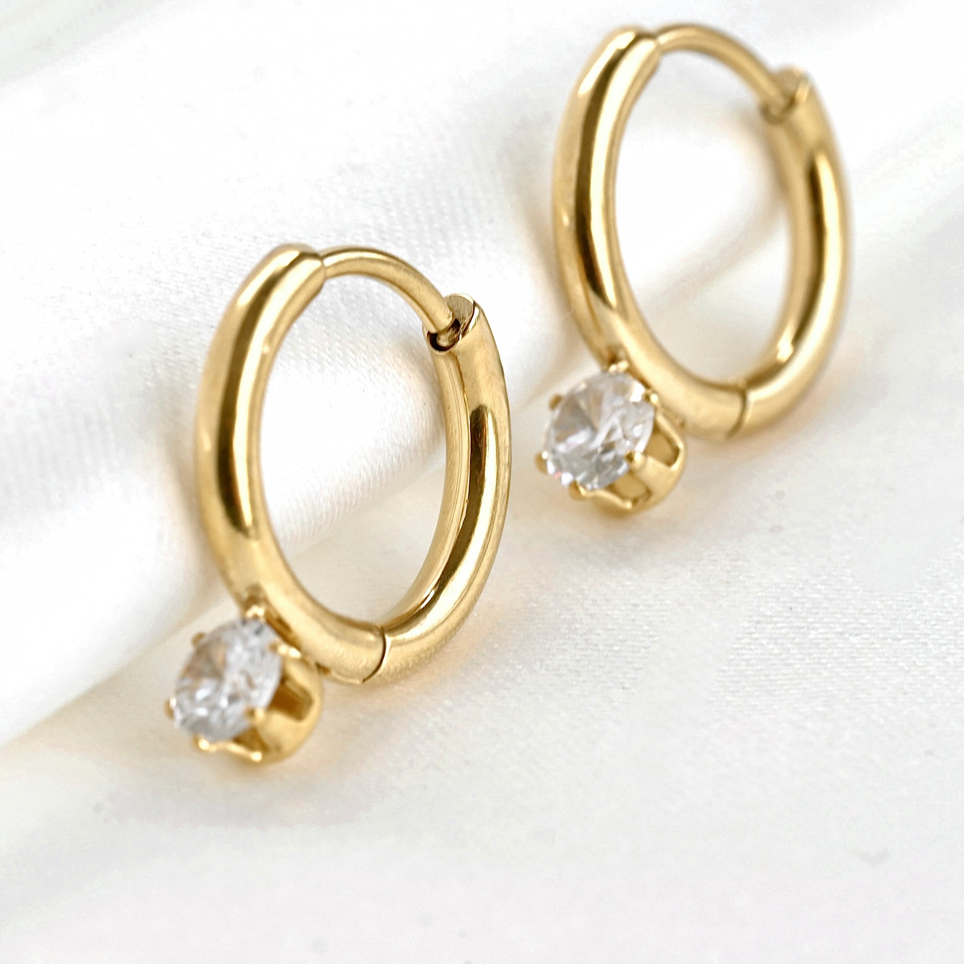 Gold hoop earrings with embedded stones in a prong setting on a white background