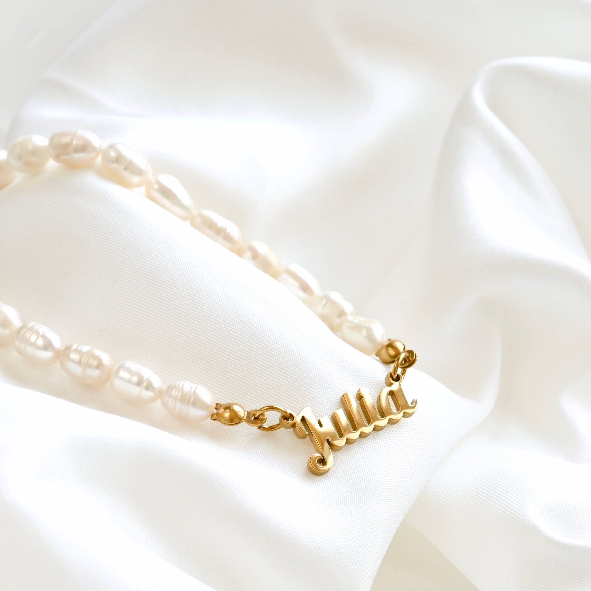 Freshwater pearl necklace with a gold nameplate on a white fabric background