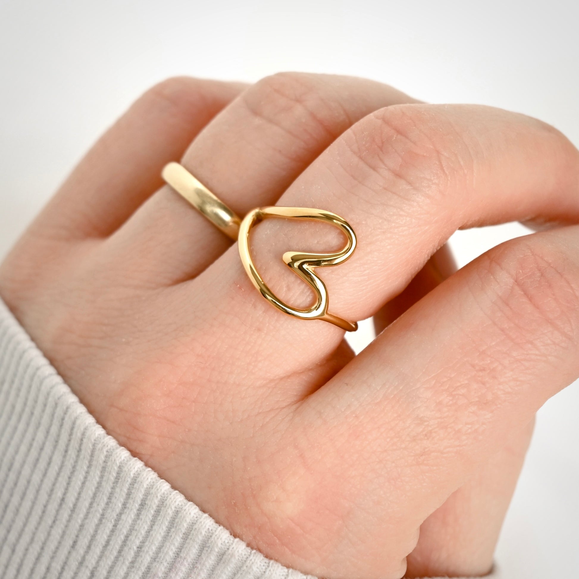 Large sideways heart ring in gold displayed on a hand .