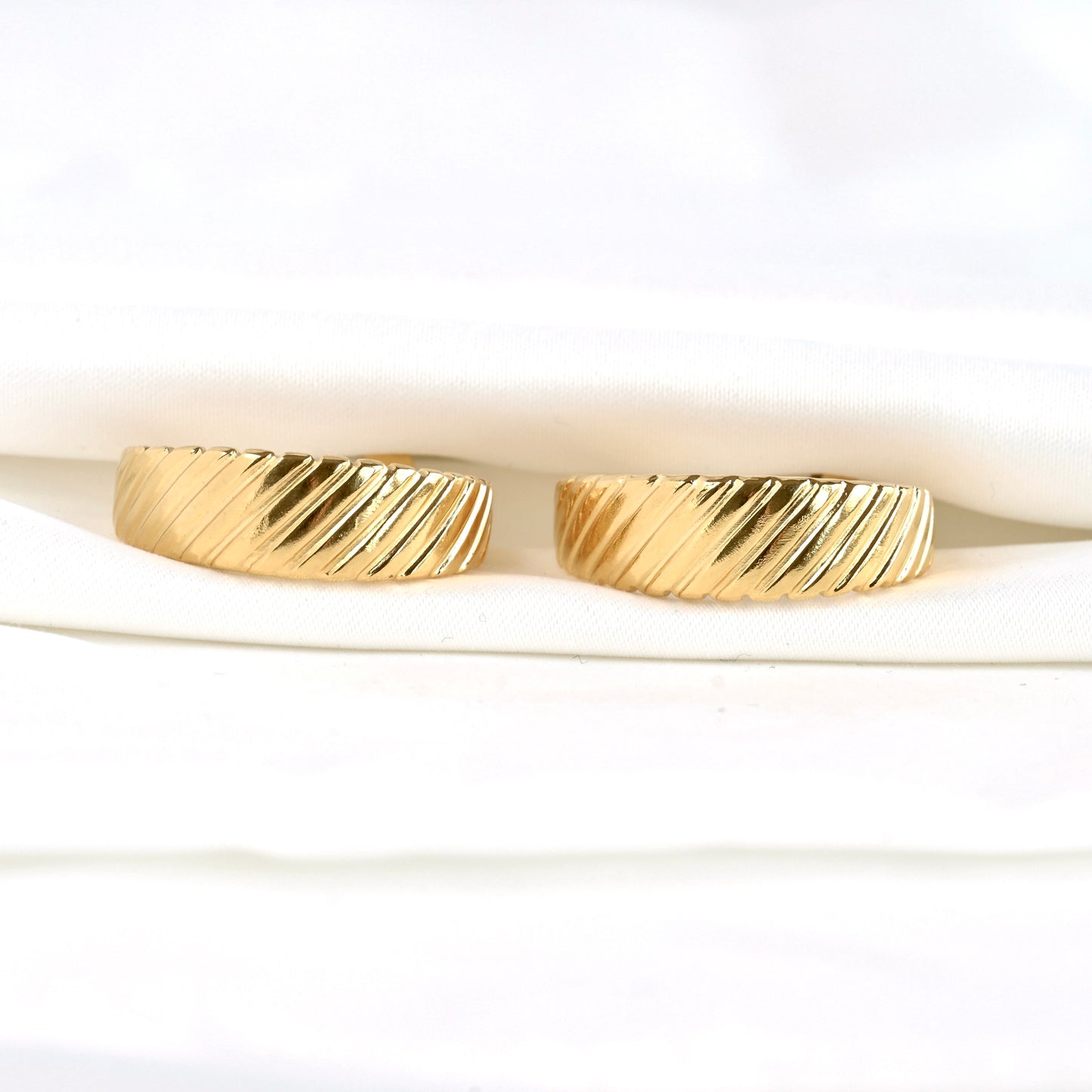 Two gold earrings with diagonal stripes on a white background