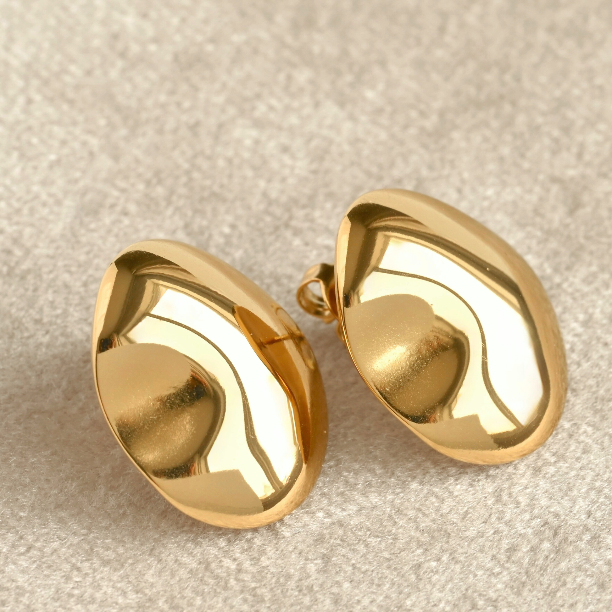 Pair of organic shaped oval gold earrings on a beige fabric background