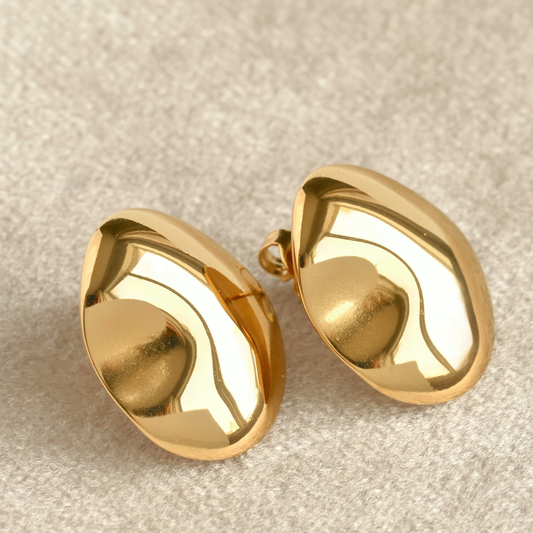 Pair of organic shaped oval gold earrings on a beige fabric background