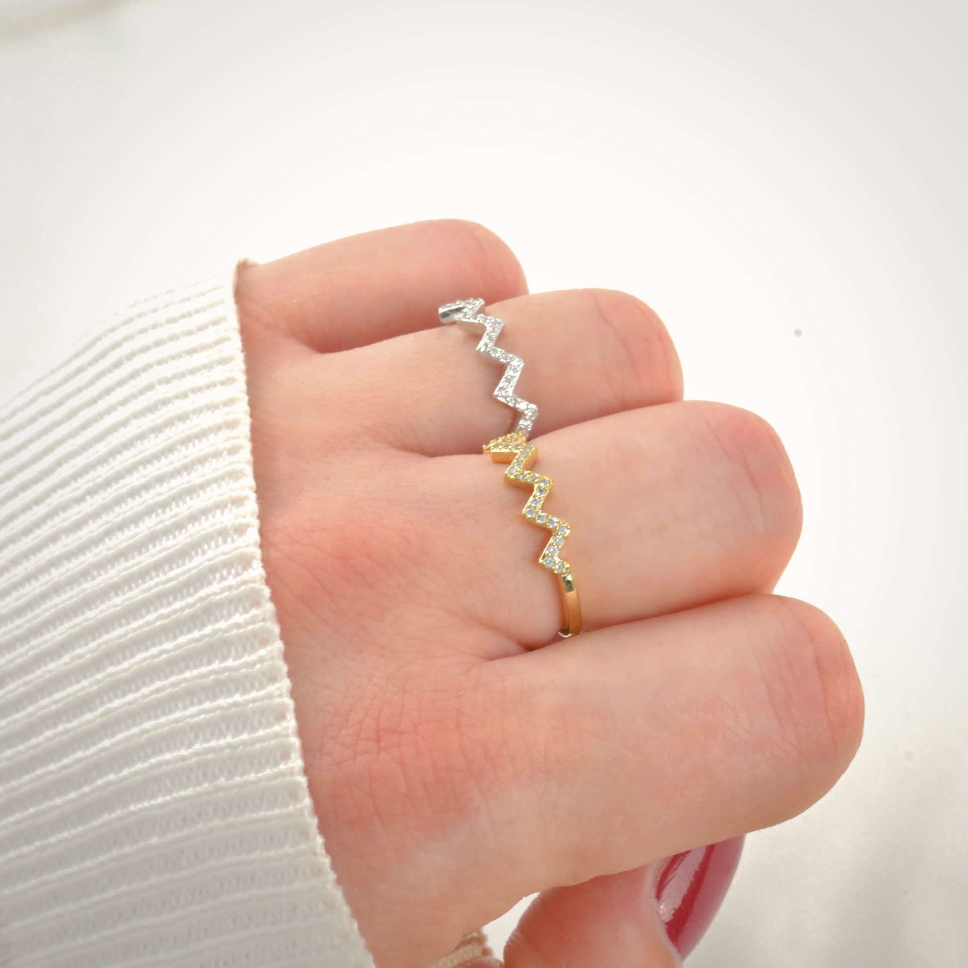 Hand wearing a gold and a silver zigzag rings pave-set with tiny CZ on a white background
