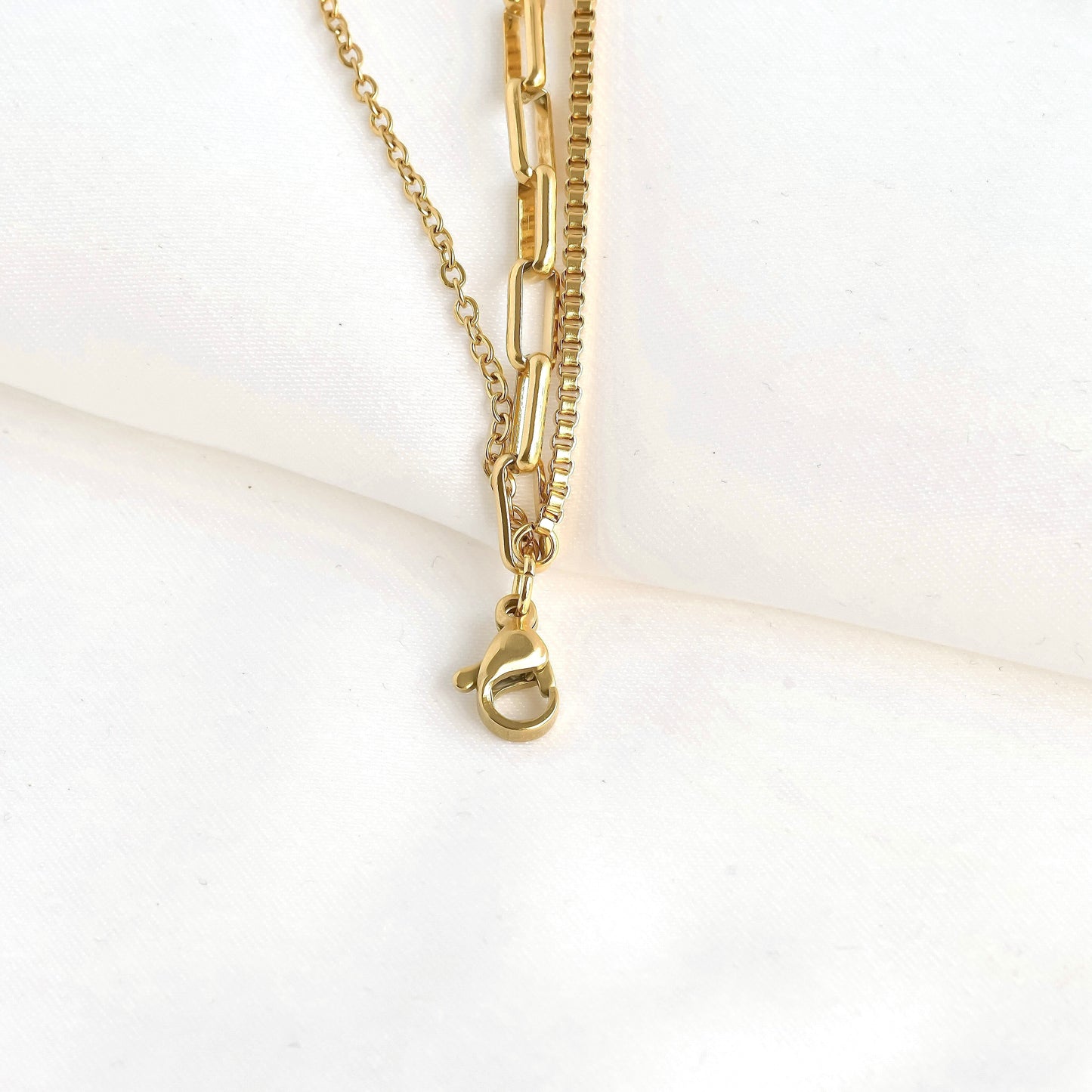 Close-up view of the clasp area of three-strand gold chain necklace showcasing that all three chains linked on a single clasp on a white background