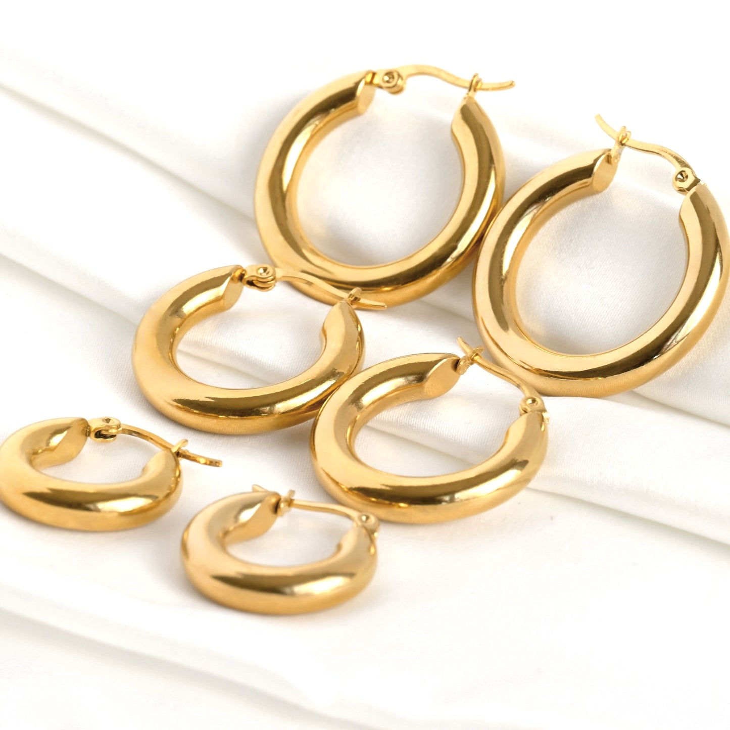 Set of gold  tunnel hoop earrings in three sizes on a white background
