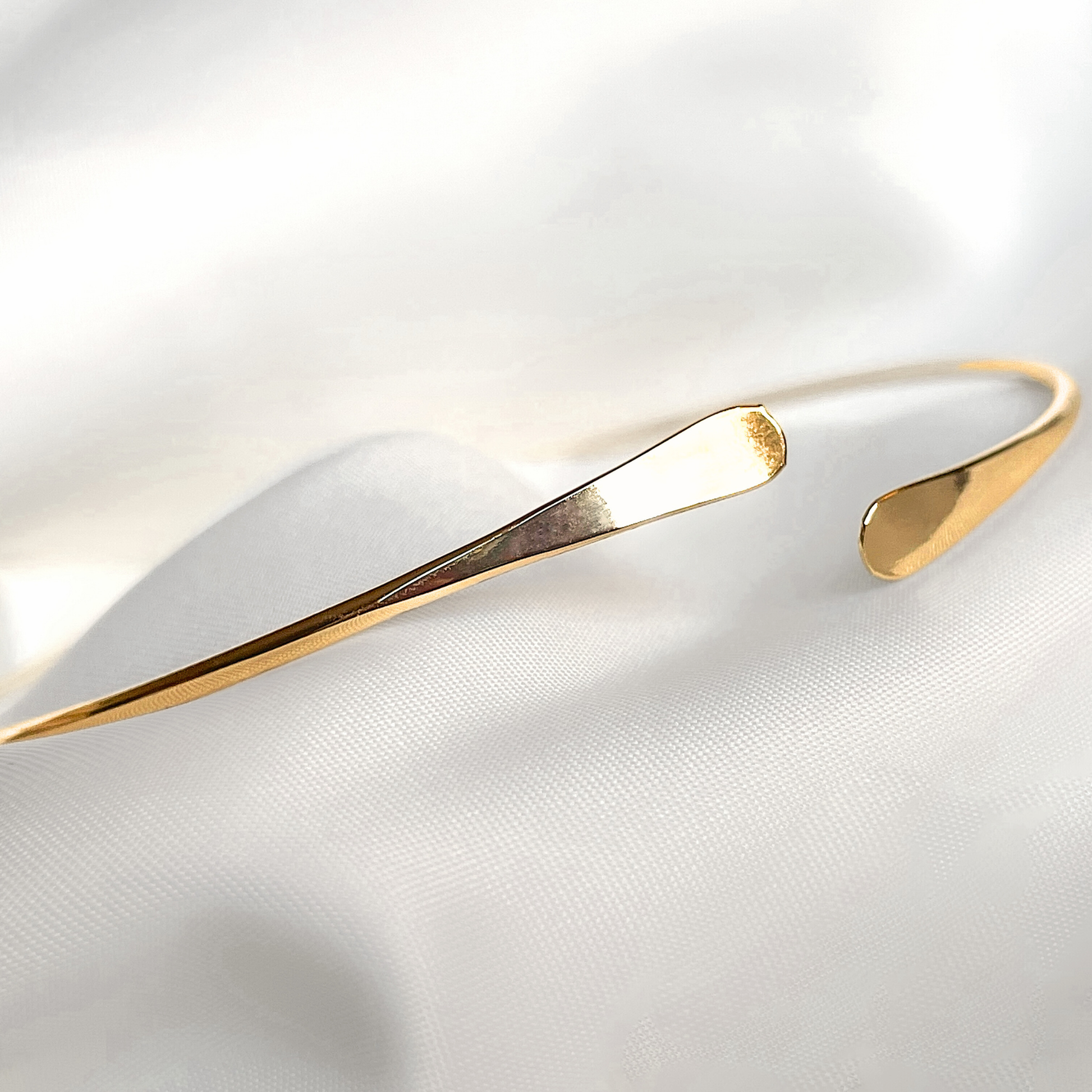 Angled front view of plus size gold cuff  bracelet on a white fabric background