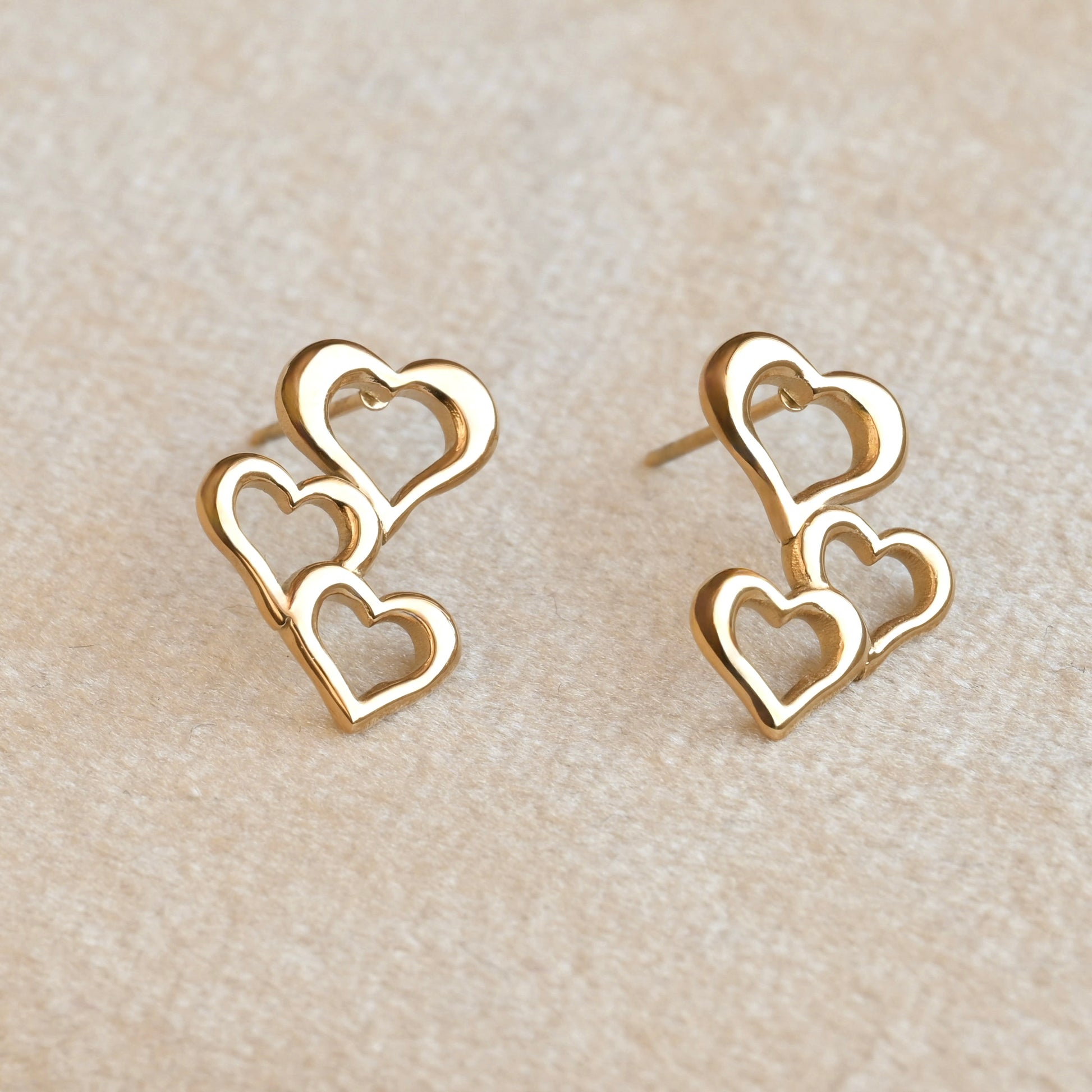 Gold heart drop earrings on a beige fabric background
