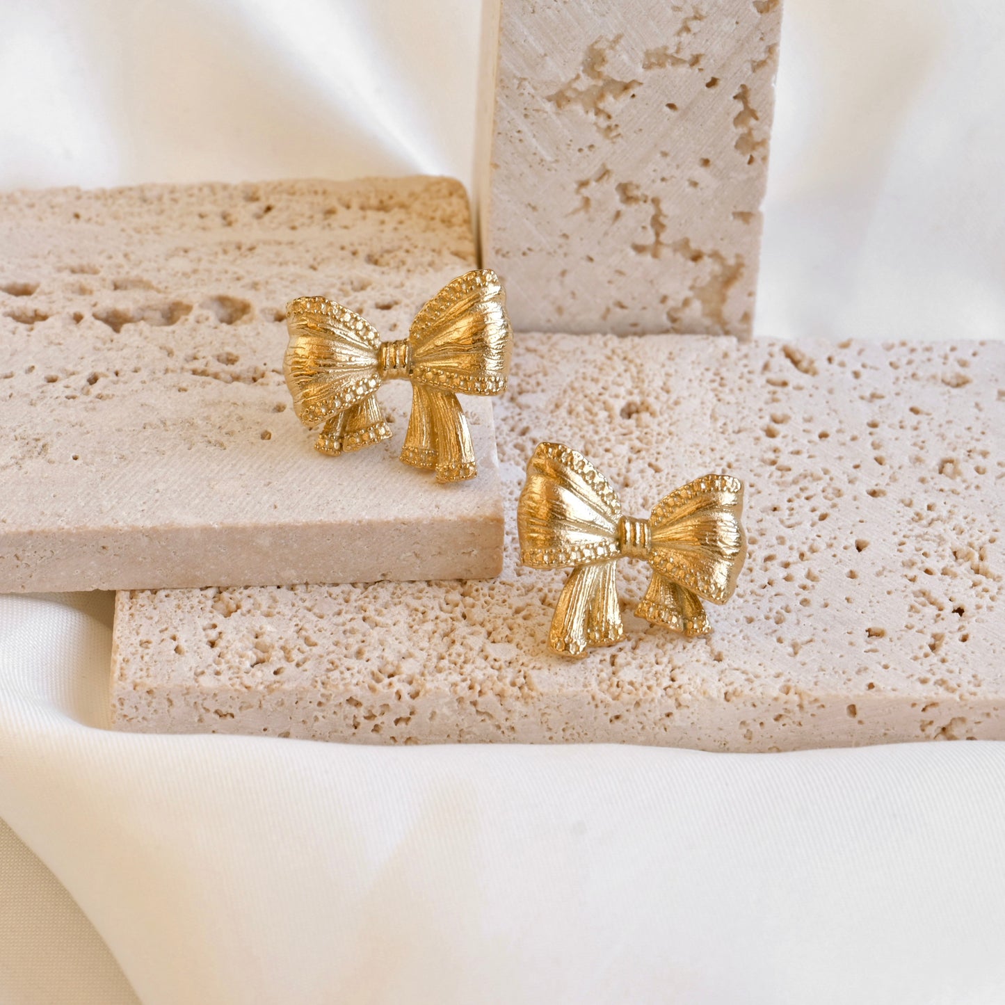 Gold bow-shaped earrings on a textured stone surface