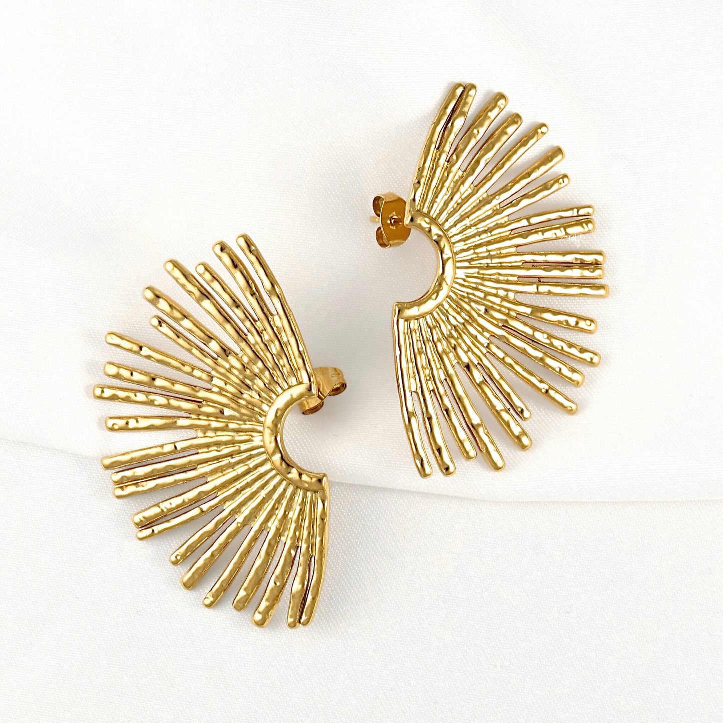 A pair of gold fan-shaped stud earrings with textured radiating bars, displayed on a clean white background.