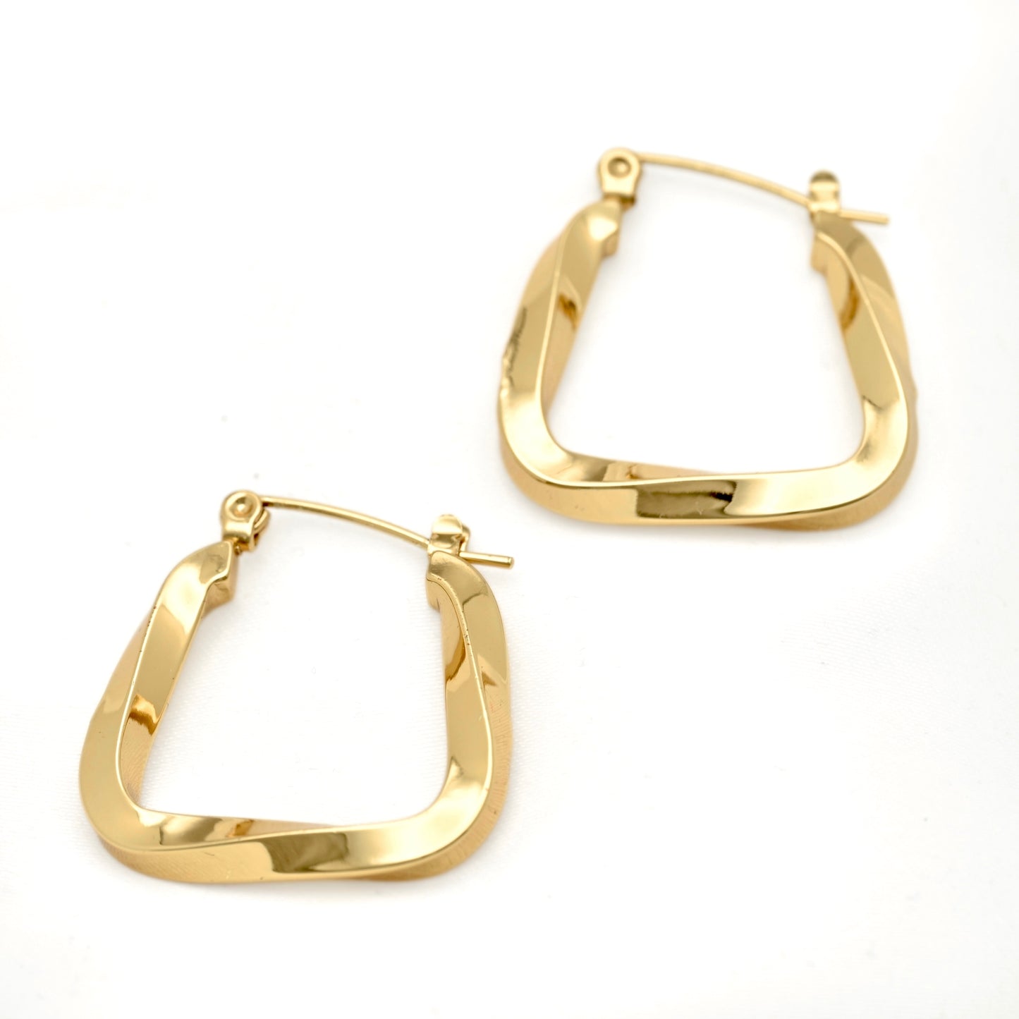 A pair of medium sized irregularly square U shaped hoop earrings with a swirling edgy design displayed on white surface