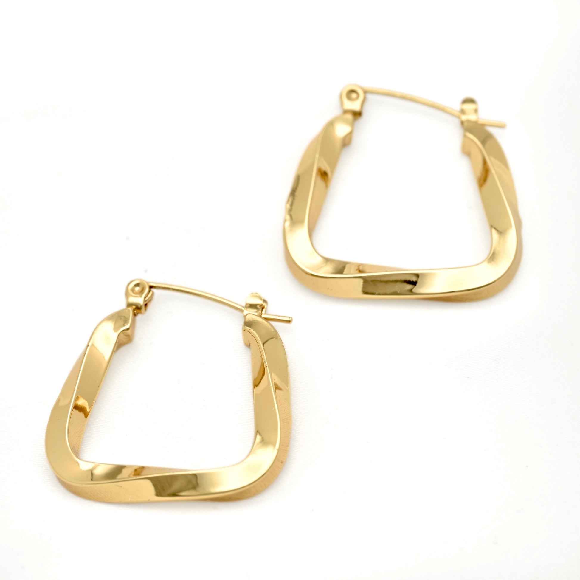 A pair of medium sized irregularly square U shaped hoop earrings with a swirling edgy design displayed on white surface