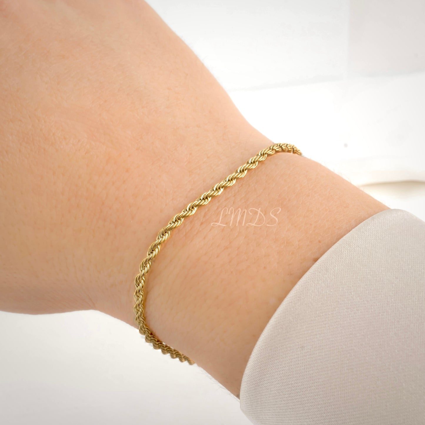 Gold rope chain bracelet on a wrist with a light background
