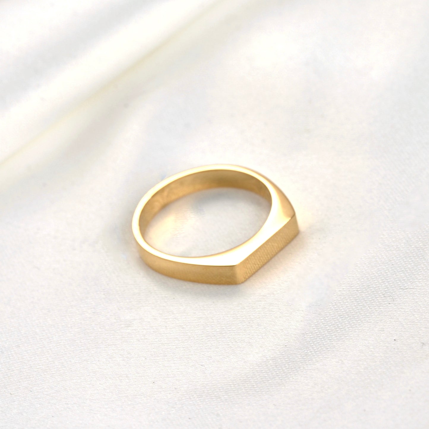 Top view of rectangular gold ring on a white fabric background