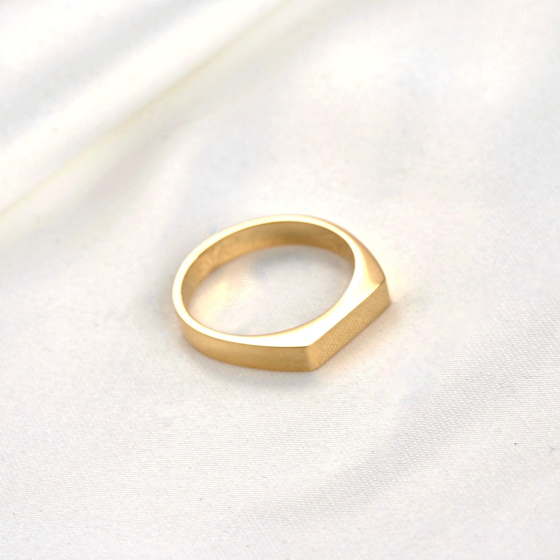 Top view of rectangular gold ring on a white fabric background