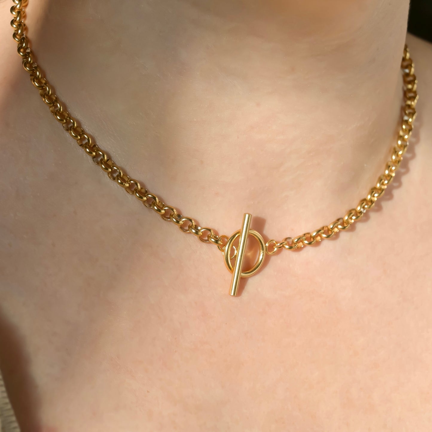 Chunky gold rolo chain necklace with a toggle clasp on a person's neck under direct sunlight