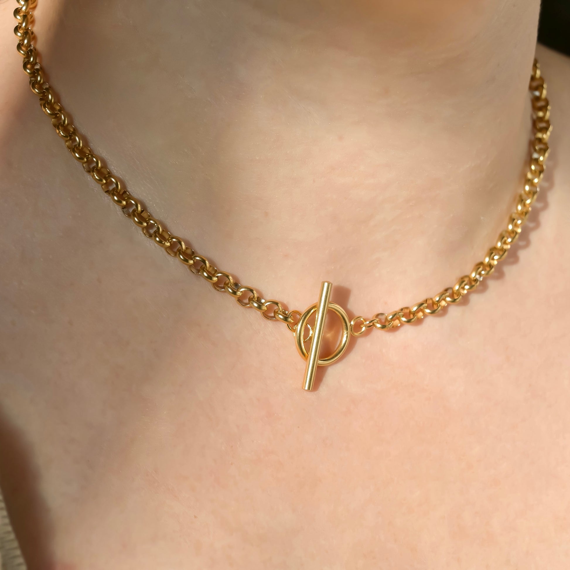 Chunky gold rolo chain necklace with a toggle clasp on a person's neck under direct sunlight