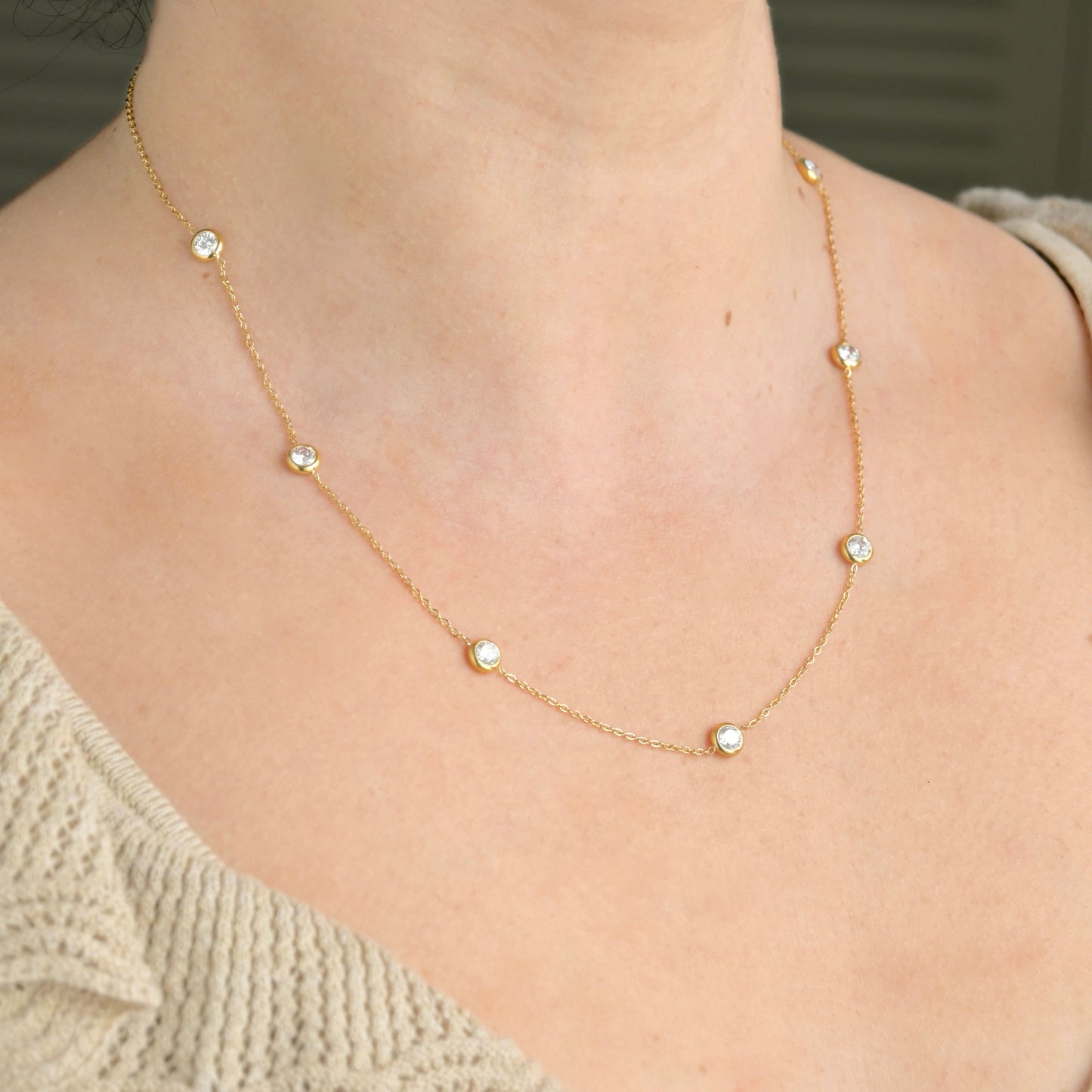 Gold necklace with bezel stations on a person wearing a beige sweater.