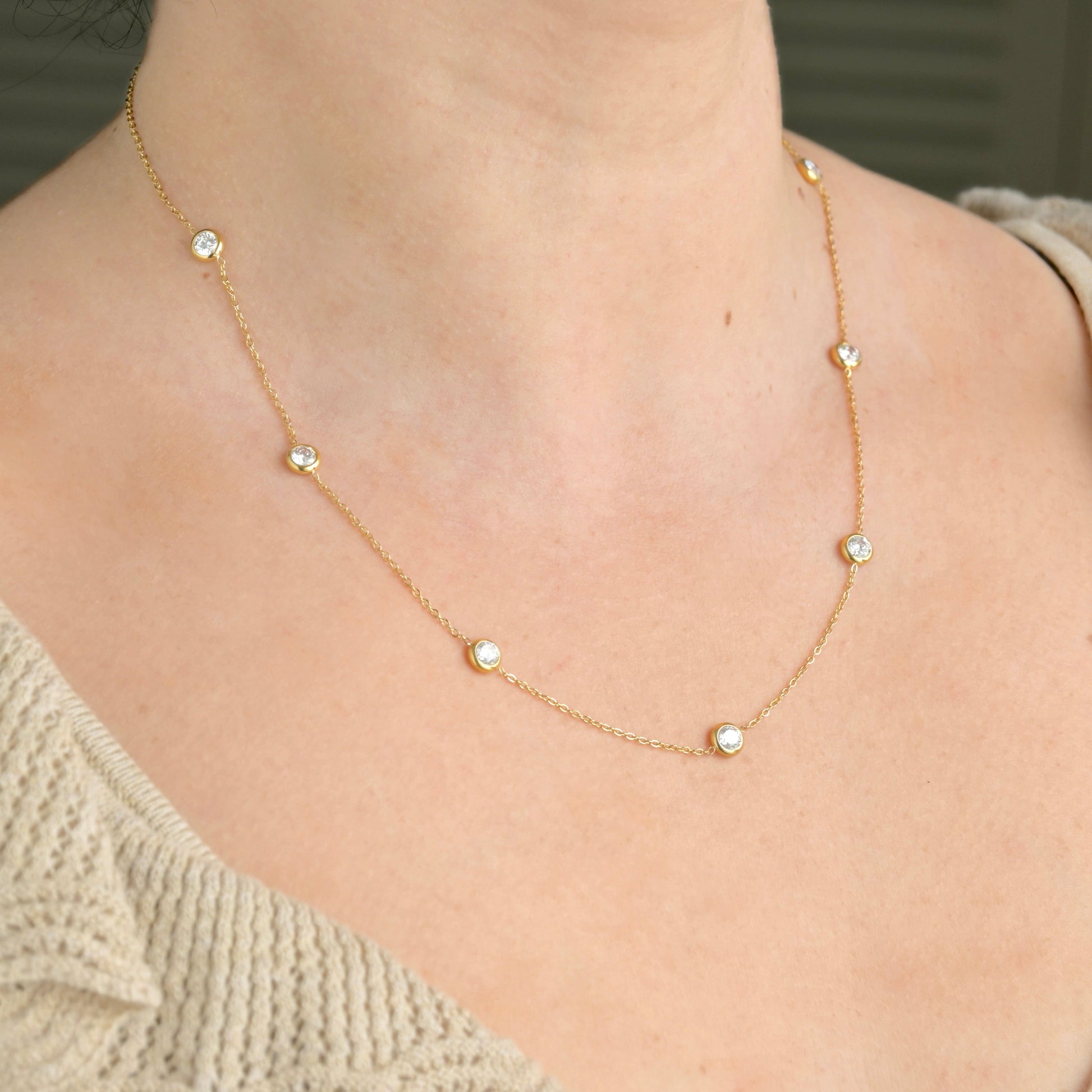 Gold necklace with bezel stations on a person wearing a beige sweater.