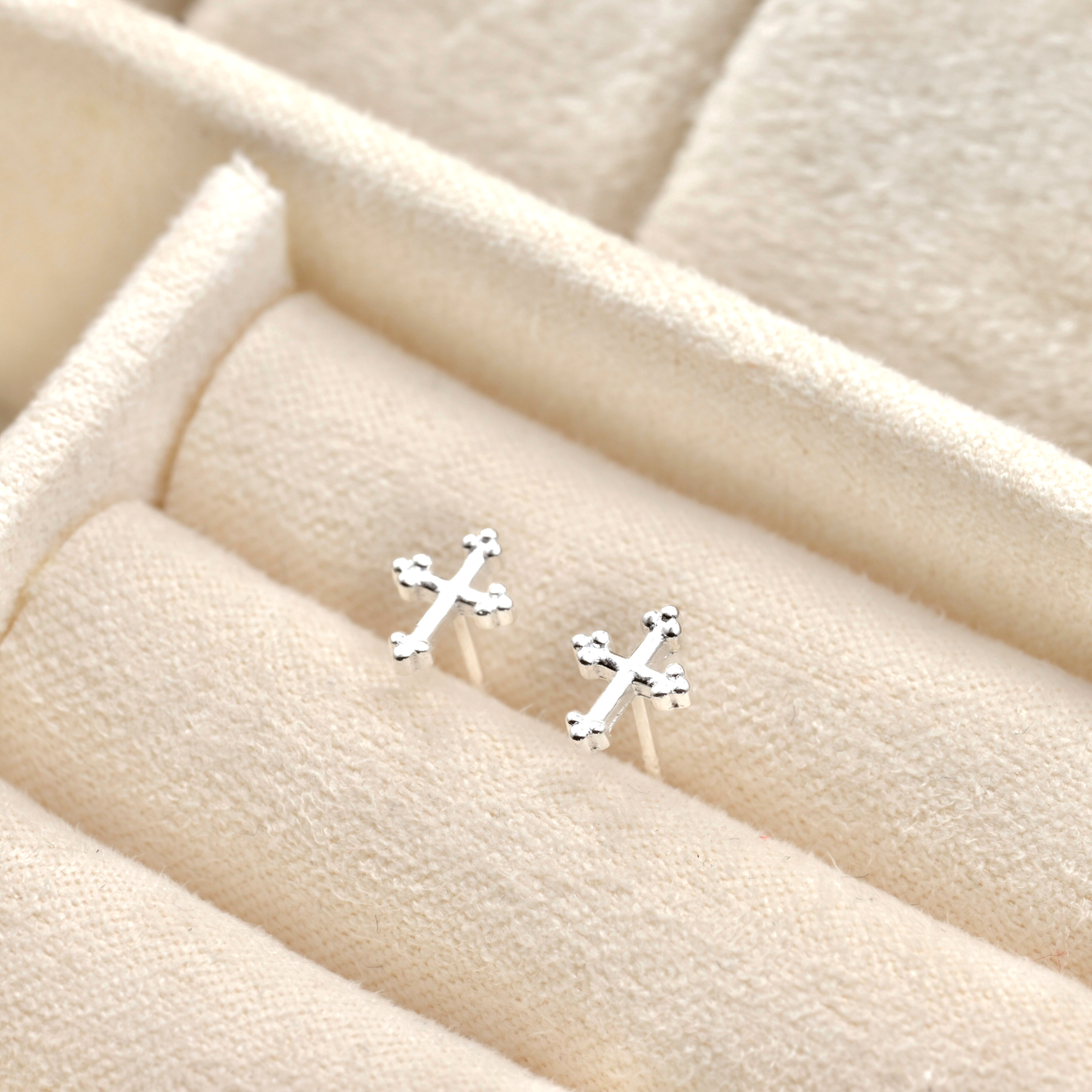 Silver cross studs on a beige fabric background