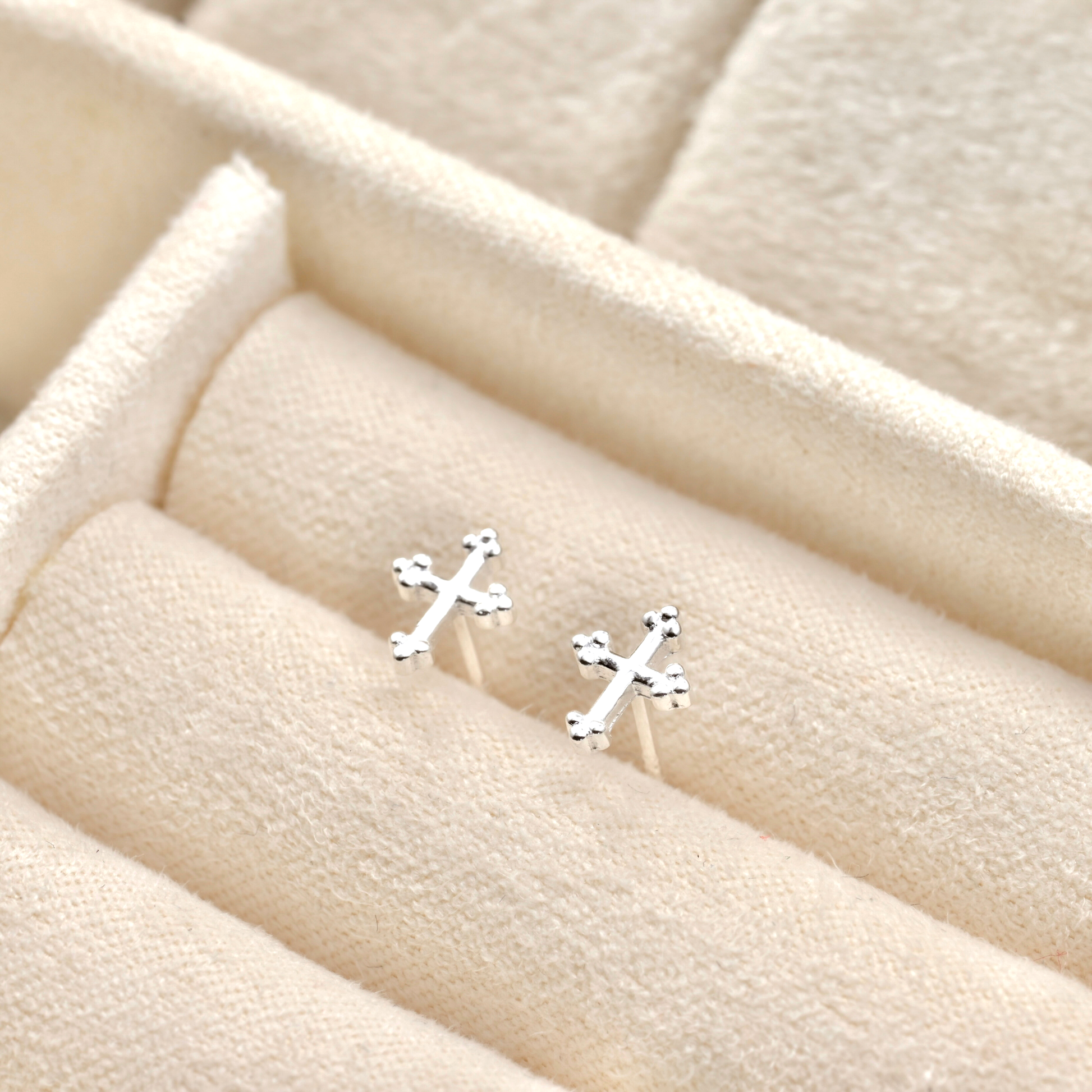 Silver cross studs on a beige fabric background