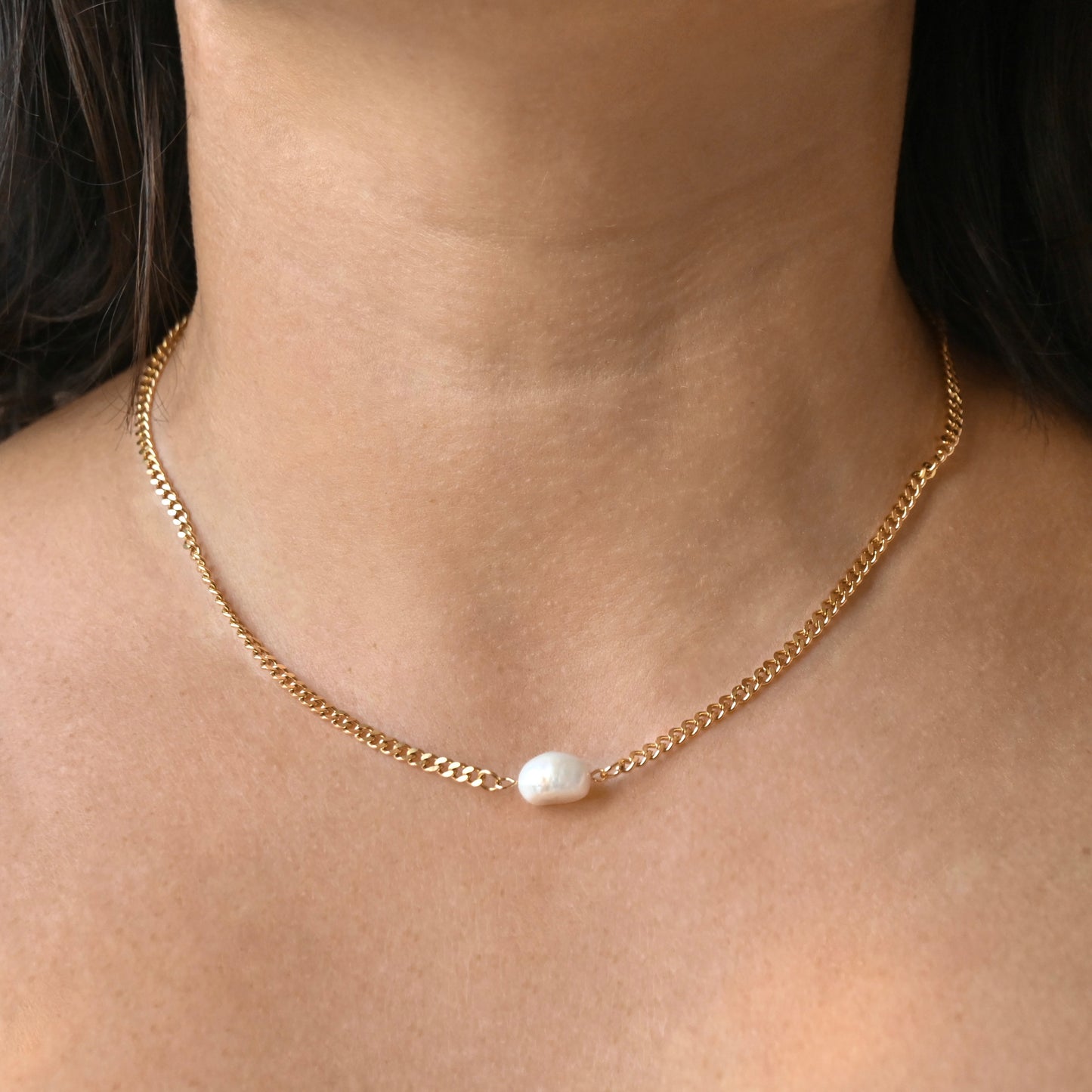 A close-up of a model's neck and collarbone wearing a delicate gold chain necklace with a single small white pearl bead at the center.