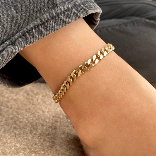 Thick gold cuban ankle bracelet on an ankle with denim jeans in the background