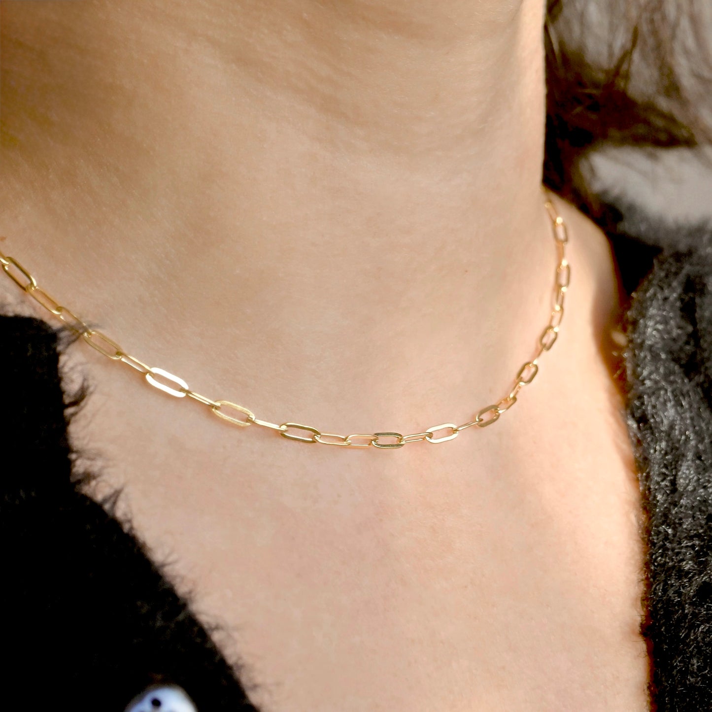 A close-up of a person's neck and upper chest wearing a delicate gold chain necklace with elongated oval links.