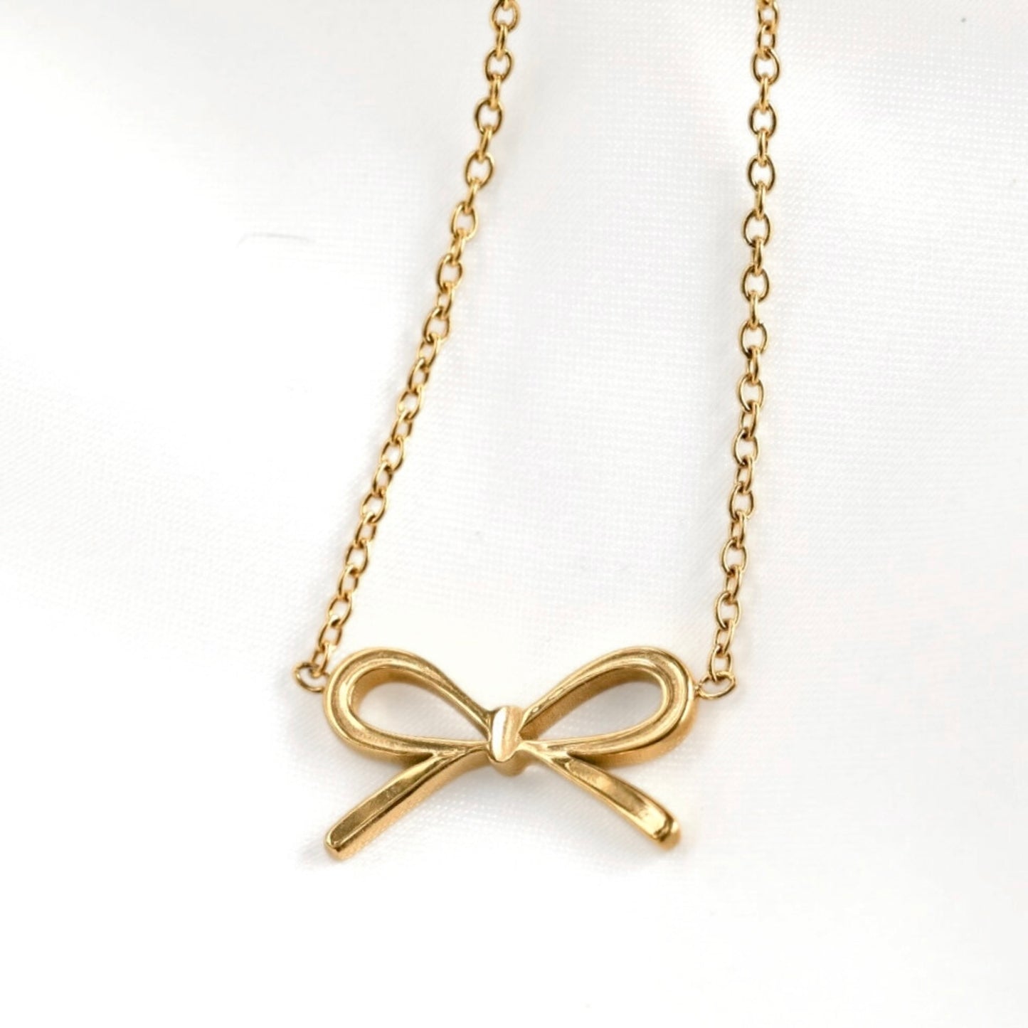 Gold bow-shaped pendant on a chain against a white background