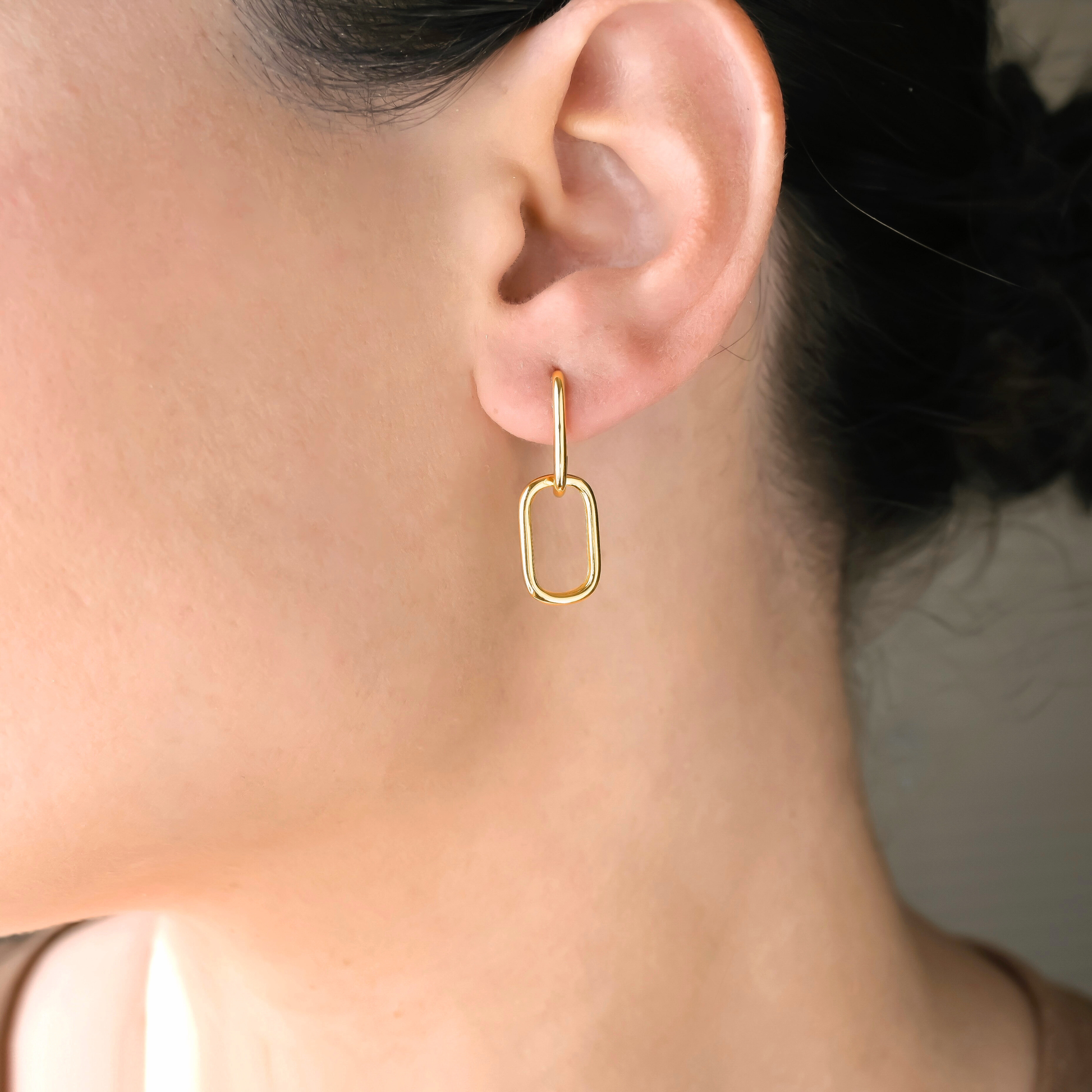 Gold interlocking U hoop earring worn by a person with a neutral background