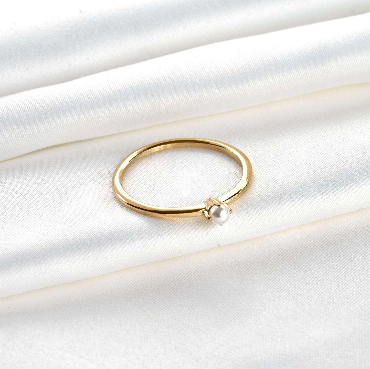 Top view of Gold pearl solitaire ring on a white satin background